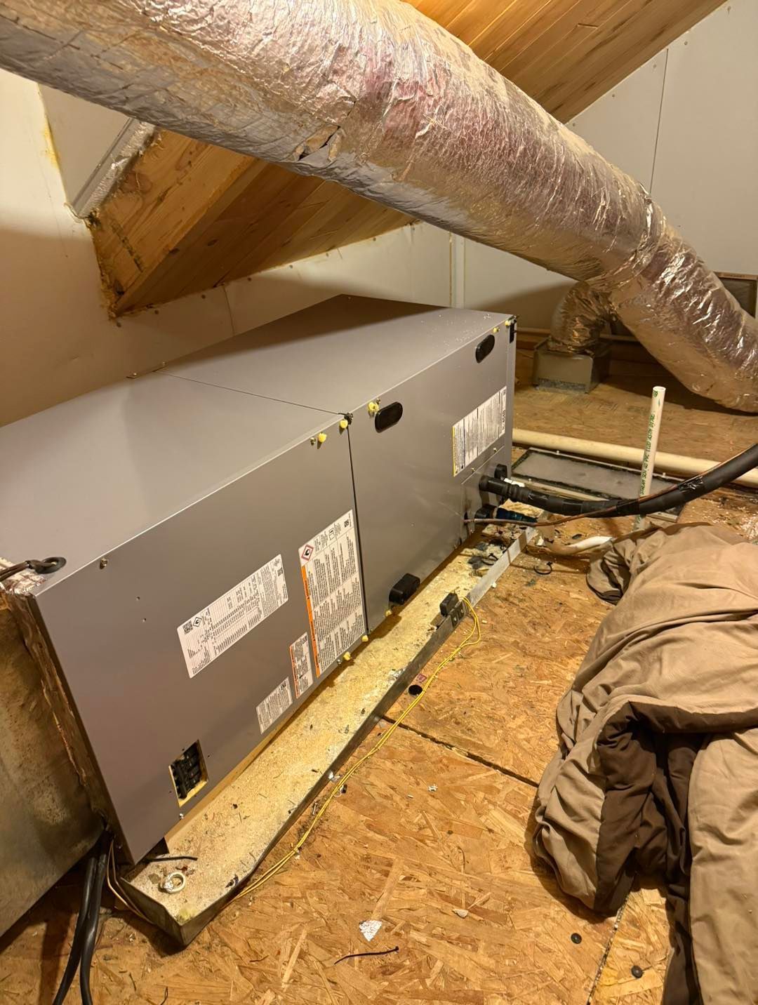 HVAC unit in an attic. Ductwork, wooden supports, and insulation are also visible.