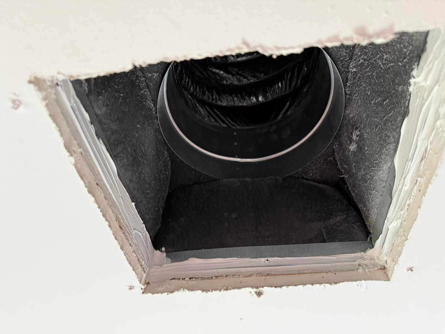 Square ceiling vent with flexible black ducting inside.