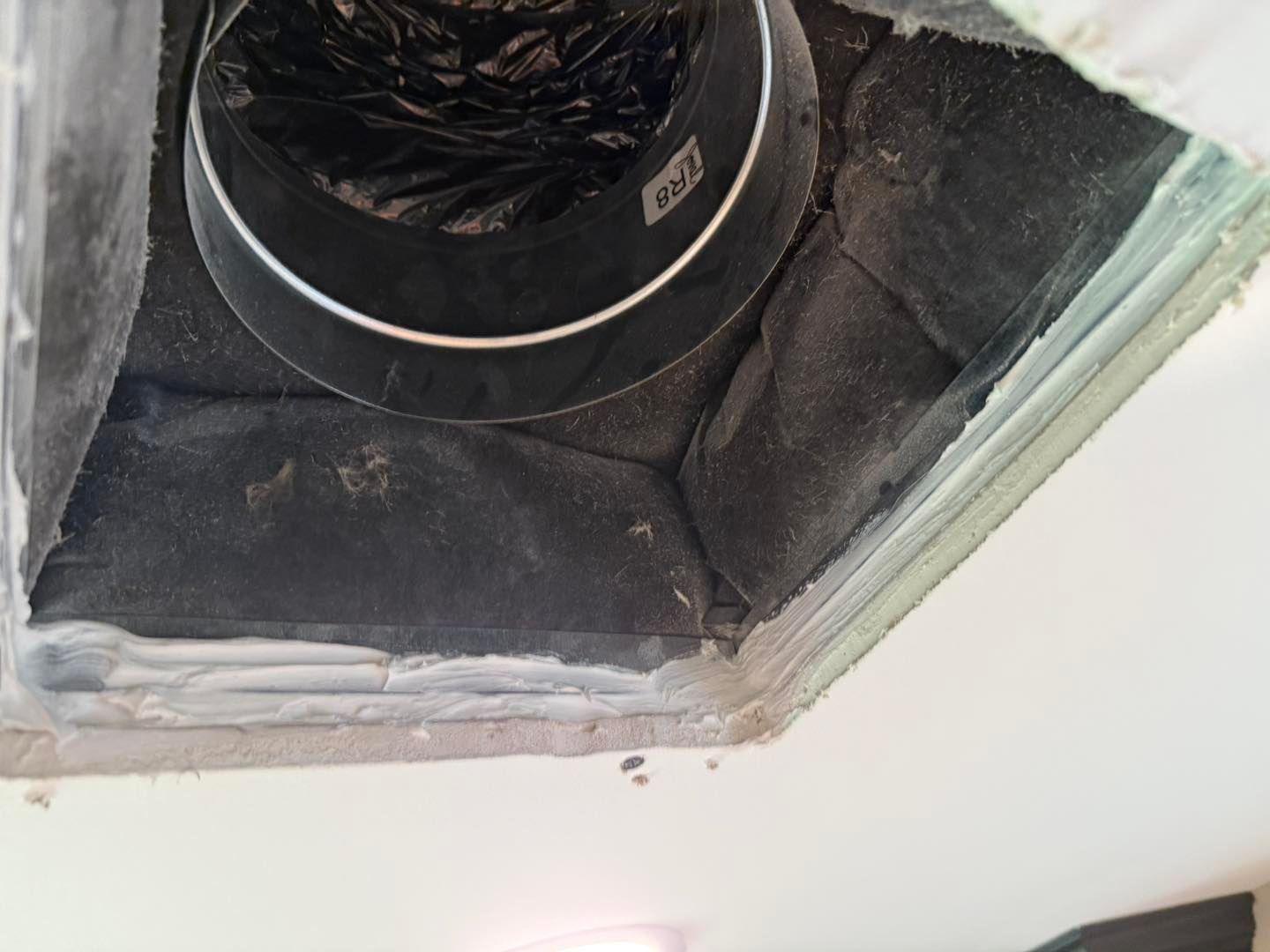 Ceiling vent with flexible ductwork, surrounded by dark insulation and white trim.