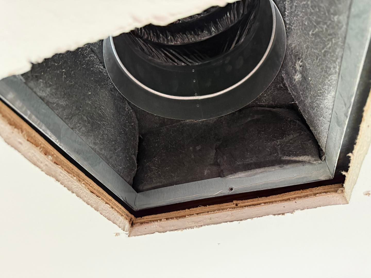 Ceiling air vent with a black duct. Dark insulation surrounds the duct, visible against the white ceiling.