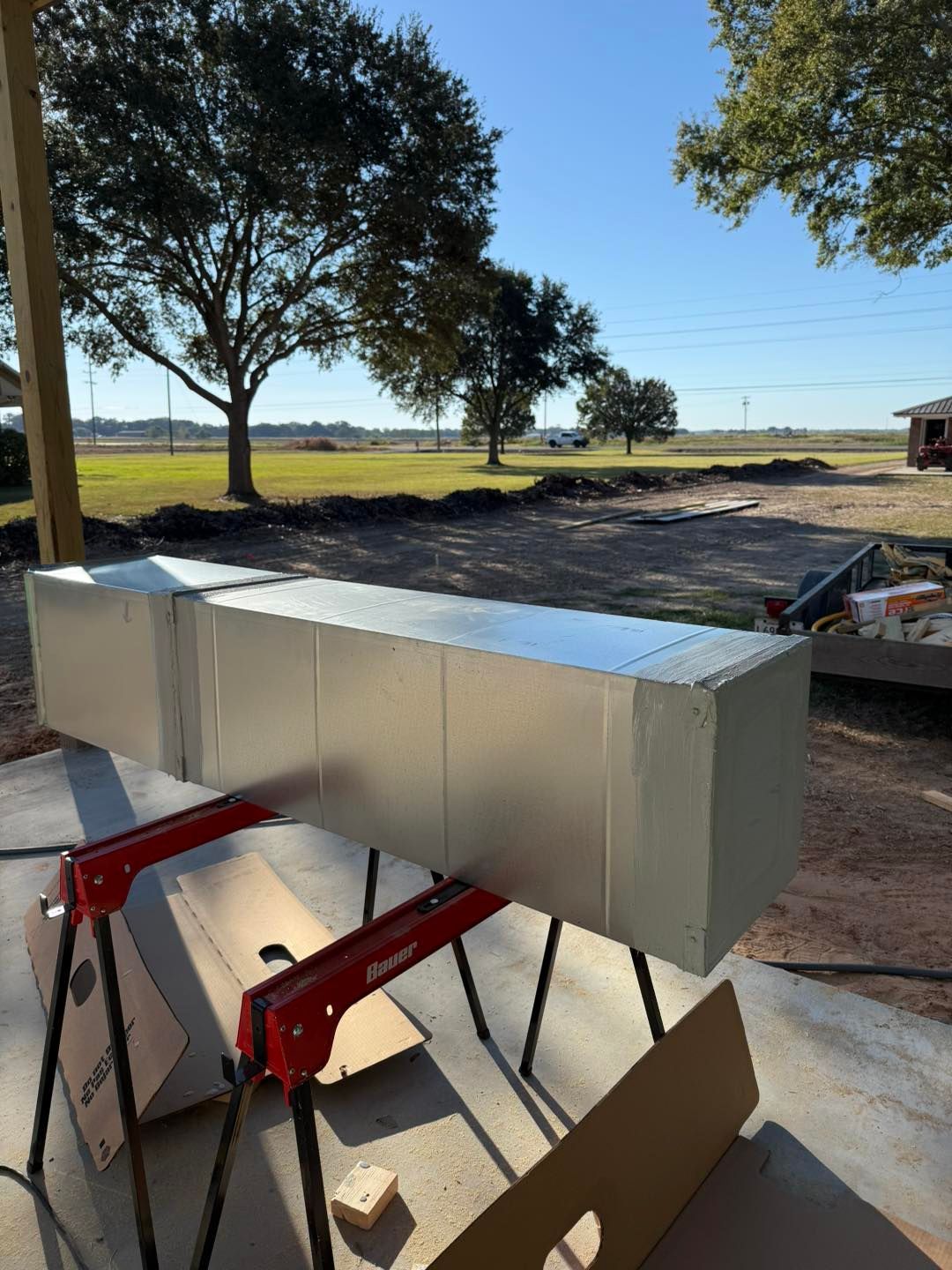 Metal HVAC ductwork on red sawhorses outdoors. Sunny day, field in background.