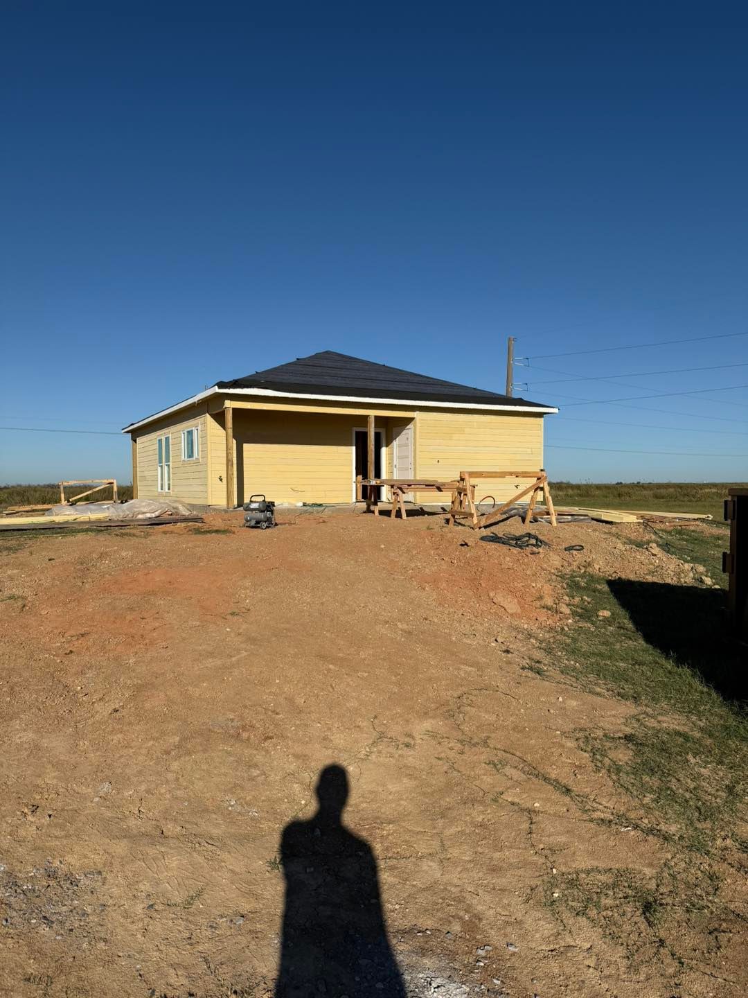A partially built house on a brown dirt lot under a clear blue sky.