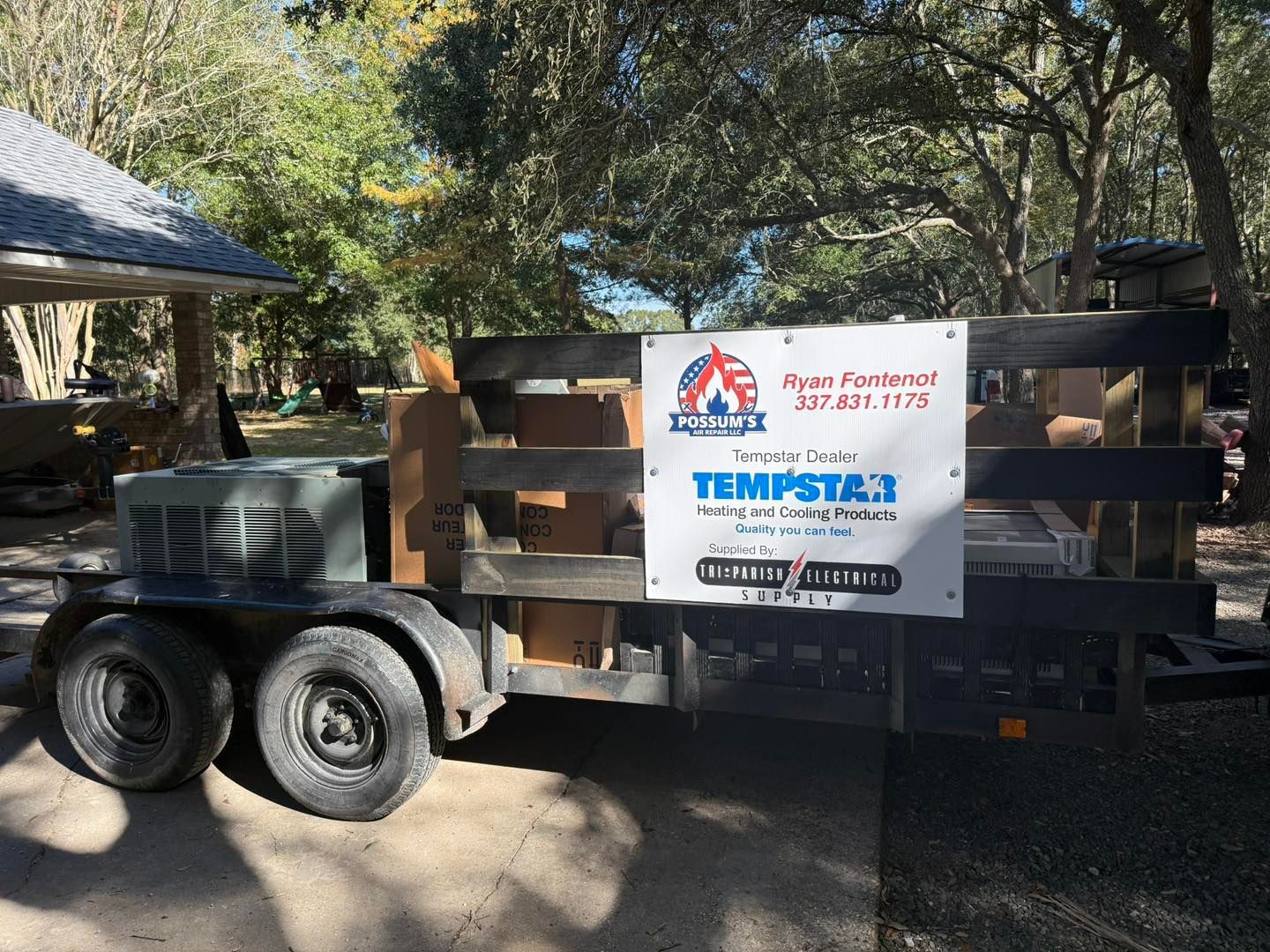 A trailer loaded with wood and a sign for Tempstar 3 HVAC service parked outside near a home.