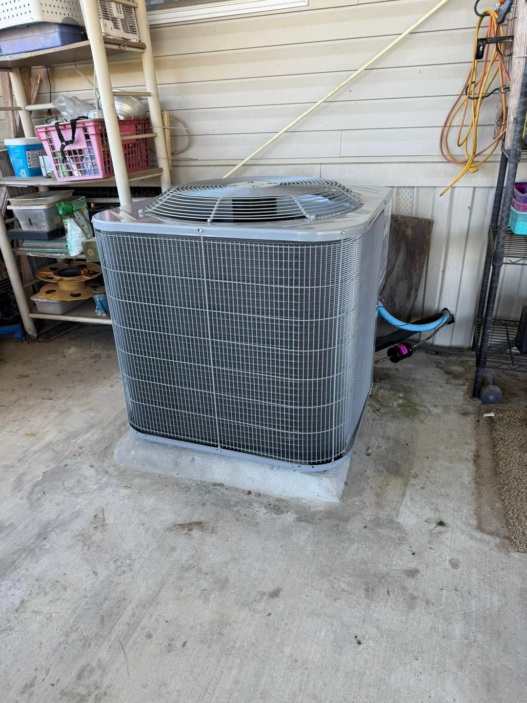 An outdoor air conditioning unit on a concrete pad with a corrugated wall backdrop.