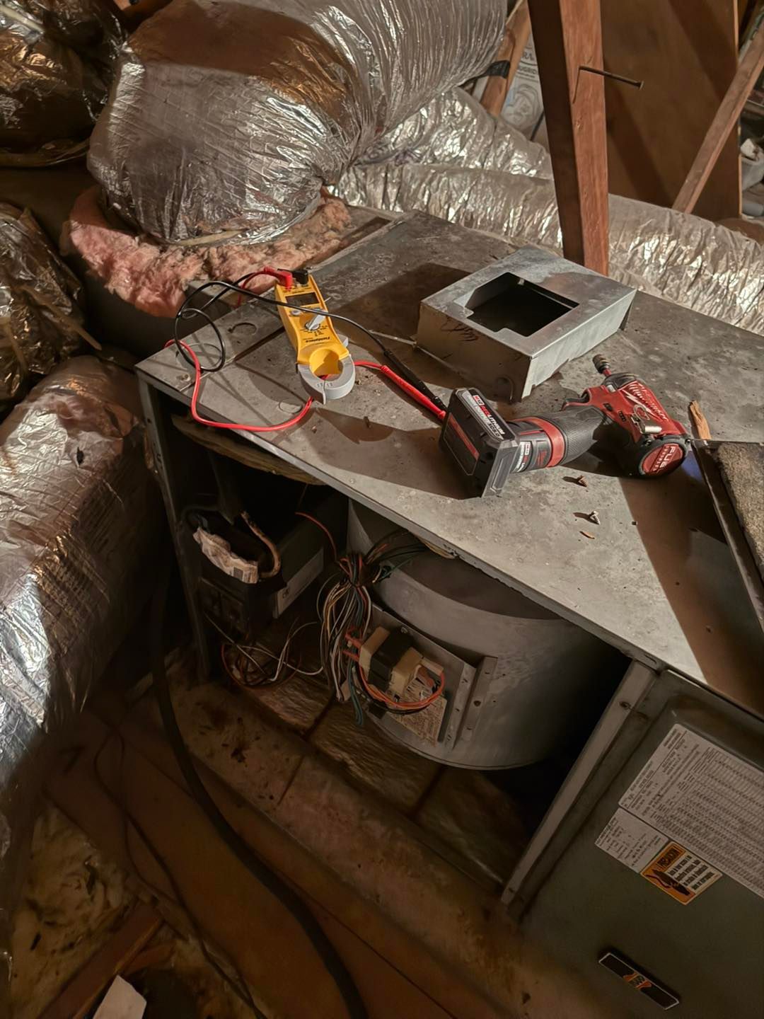 HVAC unit in an attic with tools on top, a multimeter, and ductwork.