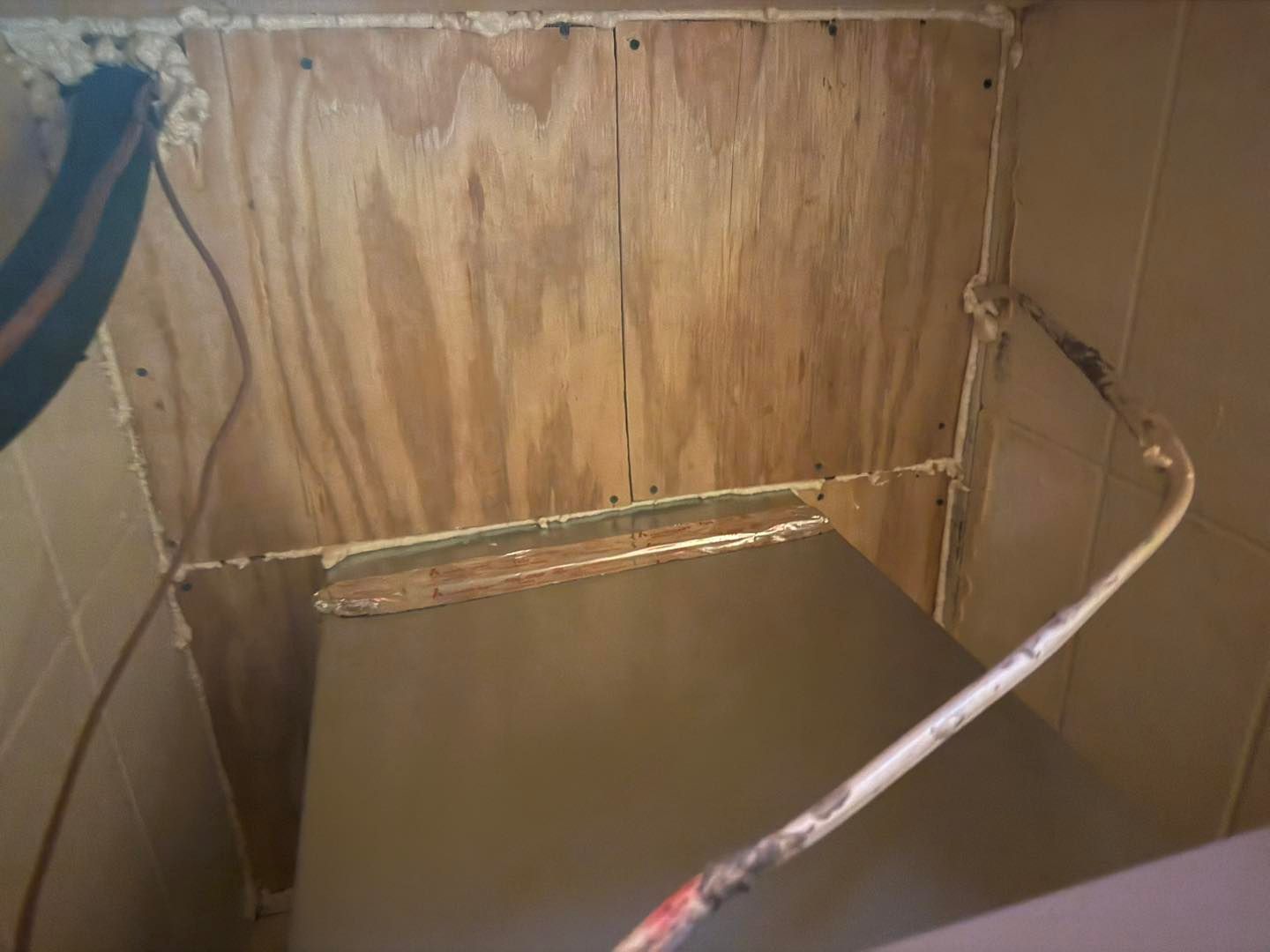 Wooden wall with a shelf, sealed with caulk. Electrical wire visible.