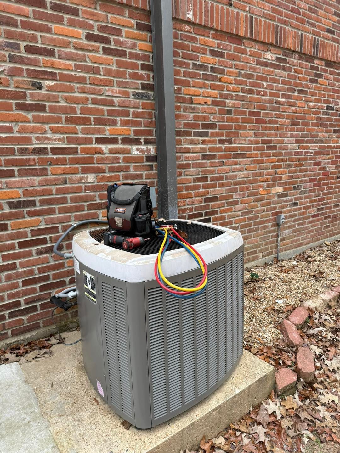 Air conditioning unit against a brick wall, with hoses attached.