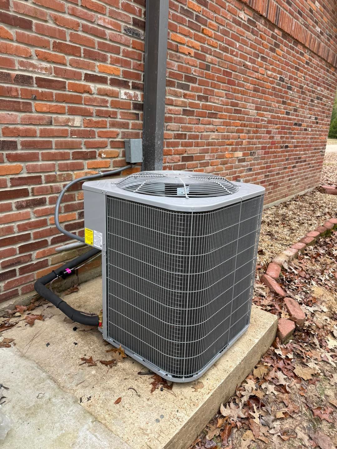Air conditioning unit sits outside a brick building on a concrete pad.