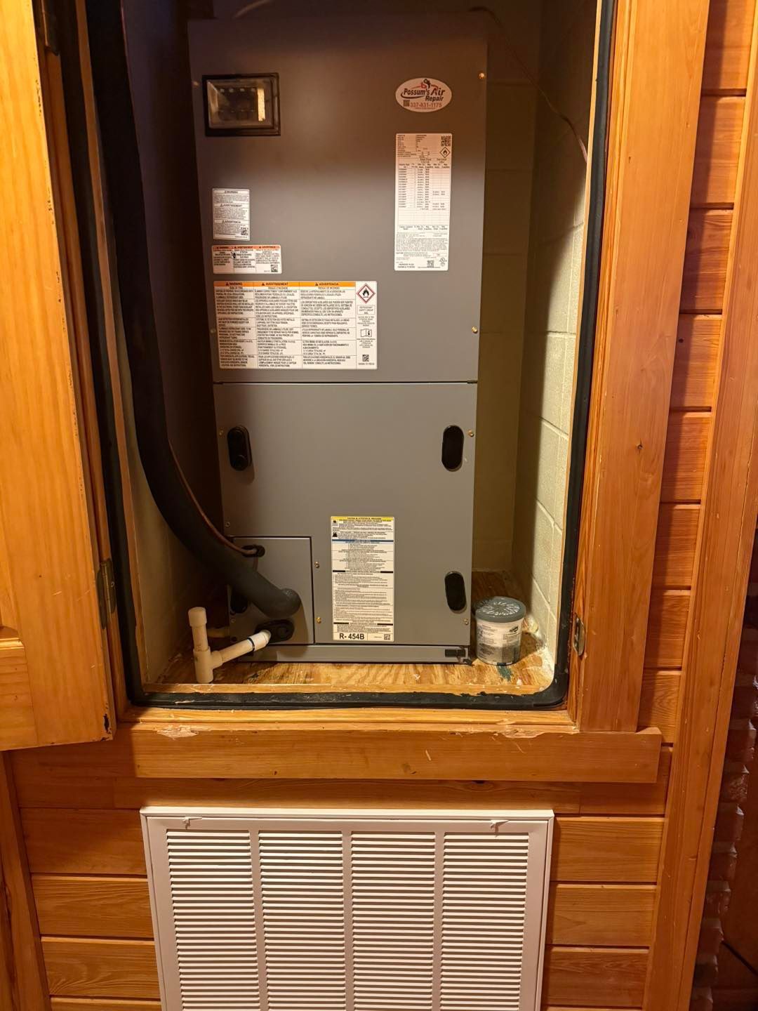 A furnace inside a wooden cabinet with a vent below.