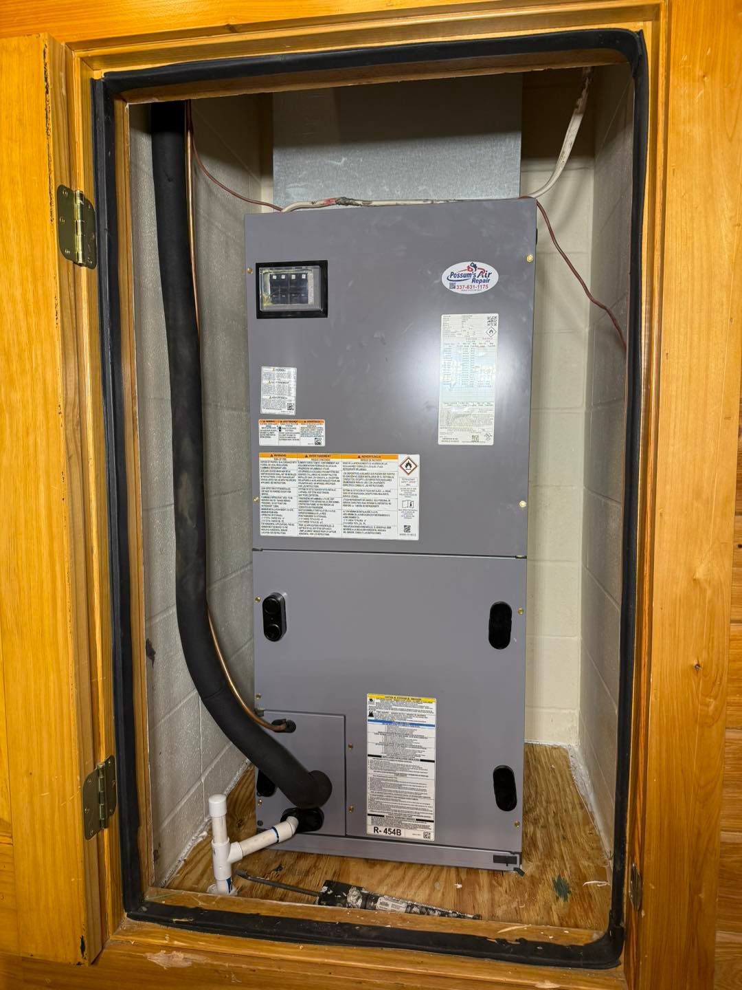 HVAC unit installed in a closet. Gray metal box with ductwork and plumbing. Wooden door frame.