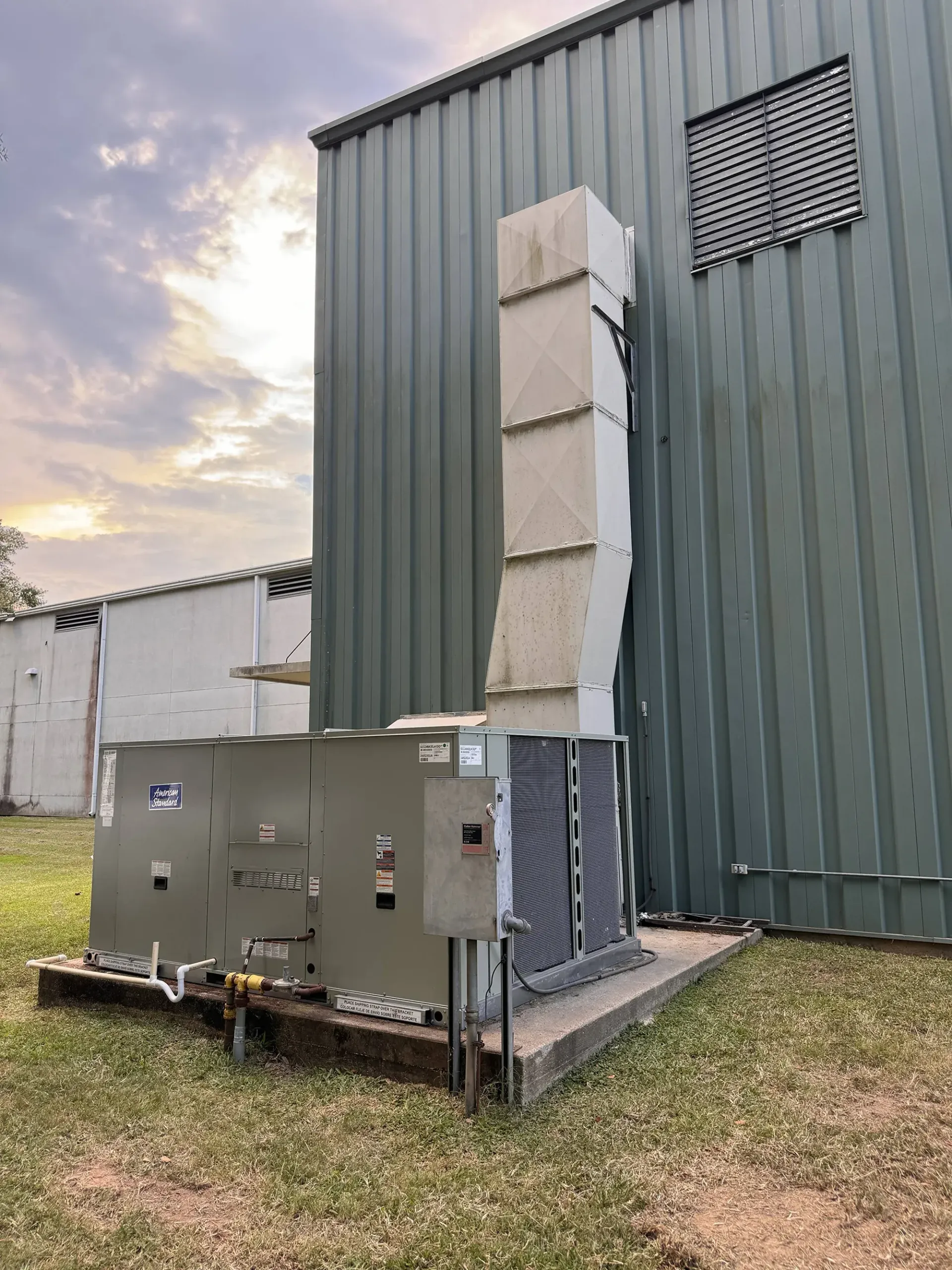 Outdoor HVAC units beside a green metal building with ductwork and vents at dusk