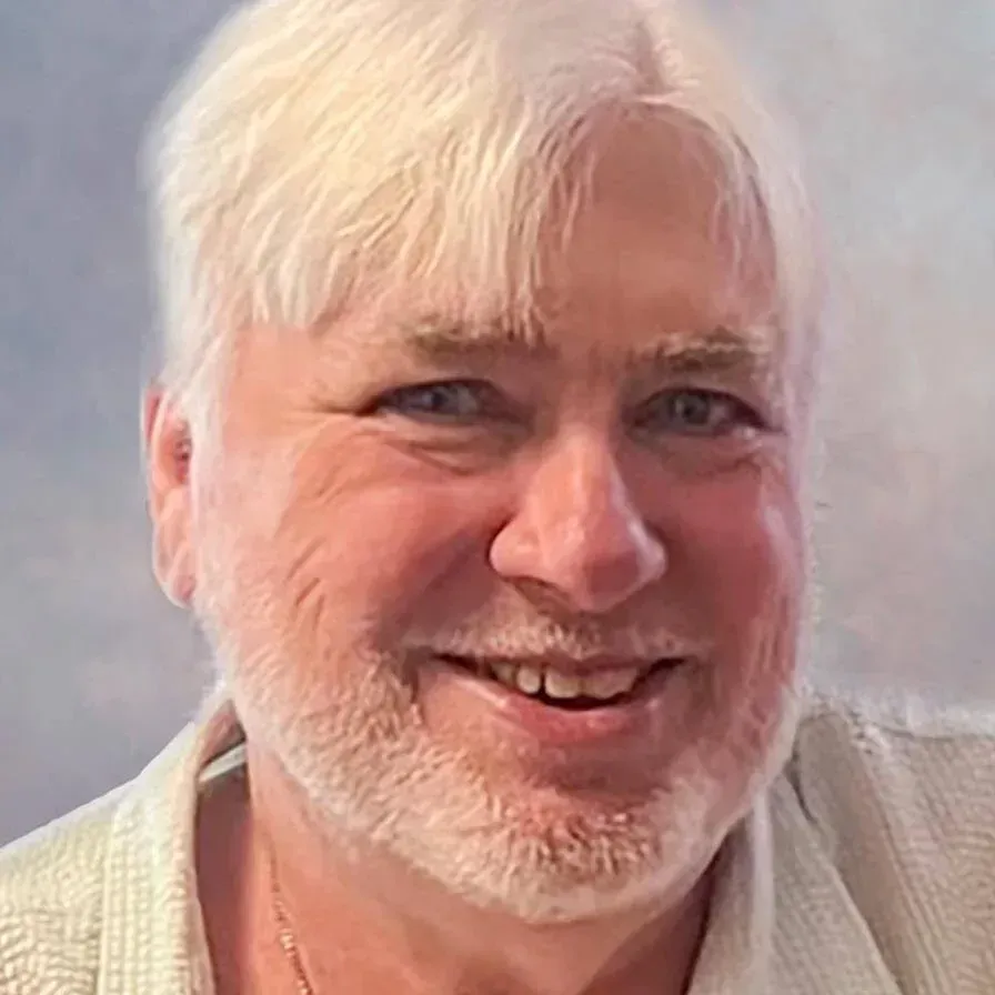 Smiling person with white hair and beard against a soft gray background