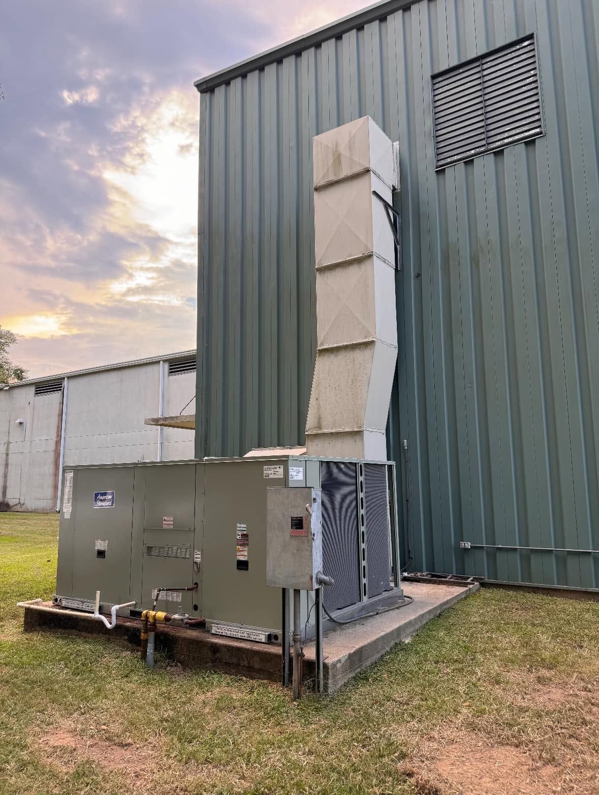 Industrial HVAC unit beside a metal building with a vertical exhaust vent at dusk