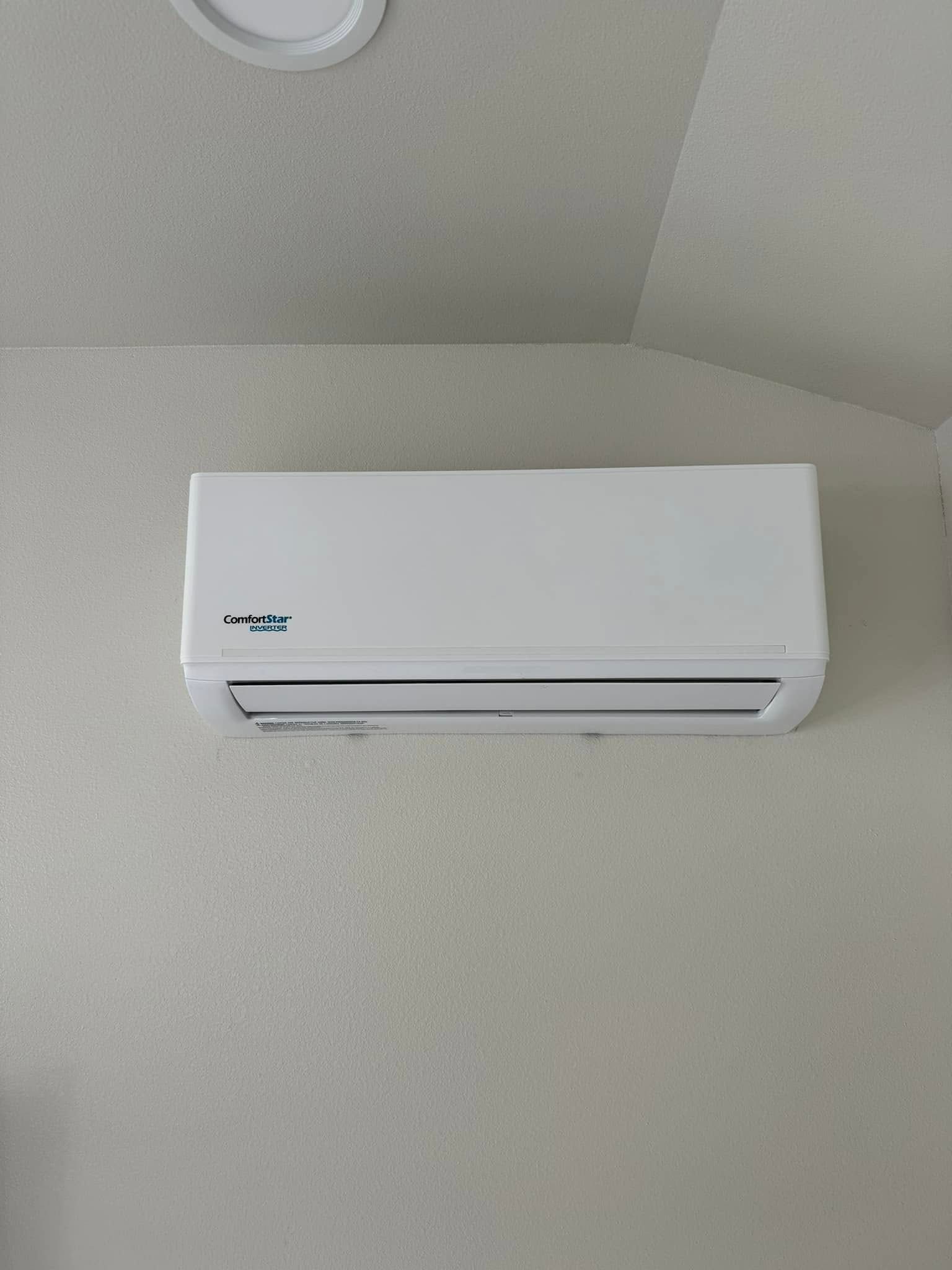 White wall-mounted air conditioner on a light gray ceiling wall.