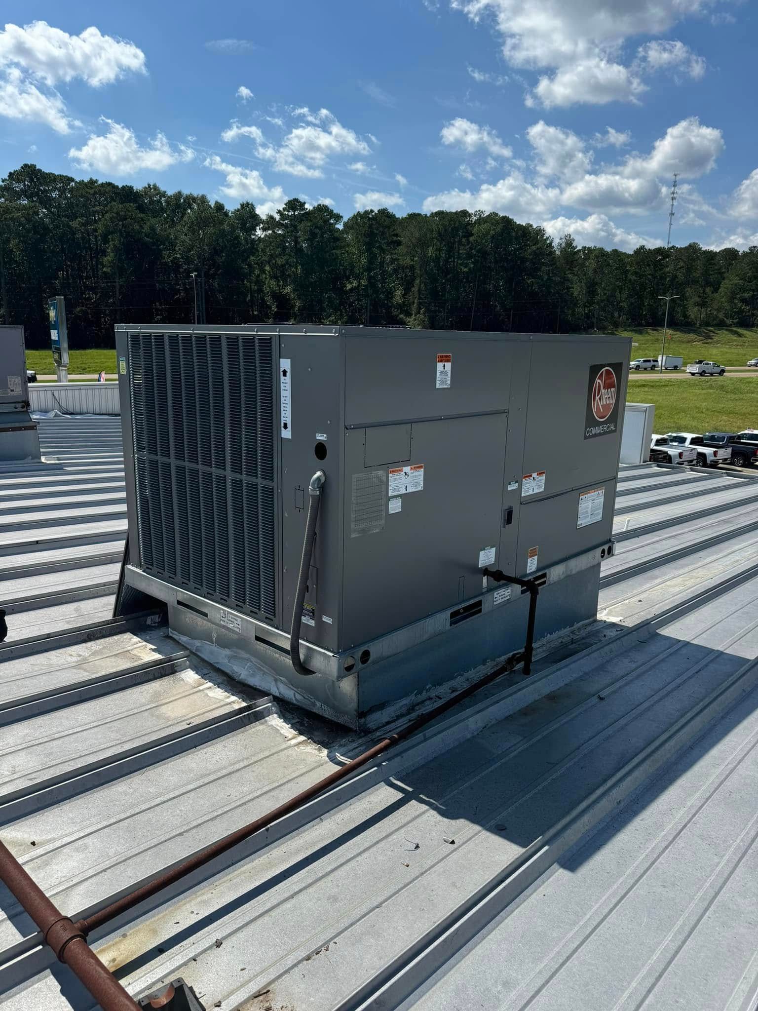 Gray rooftop HVAC unit on a metal roof under a blue sky, with trees in the background
