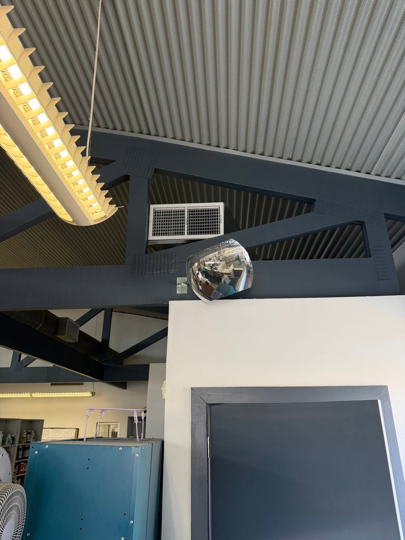 Indoor industrial ceiling with fluorescent lights, ventilation ducts, and a mirrored disco ball above a white structure