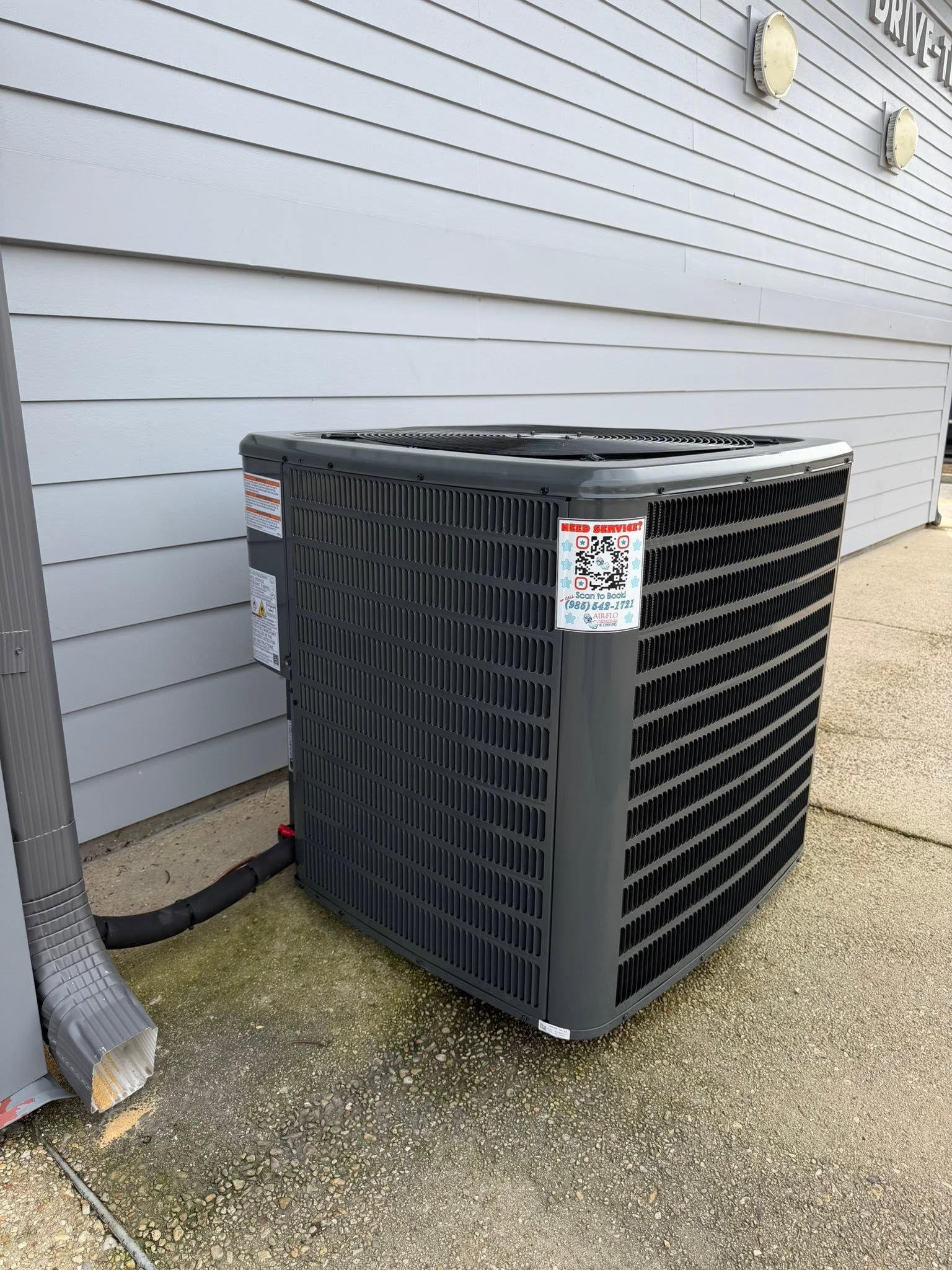 Outdoor central air conditioning unit beside a house wall on a concrete patio