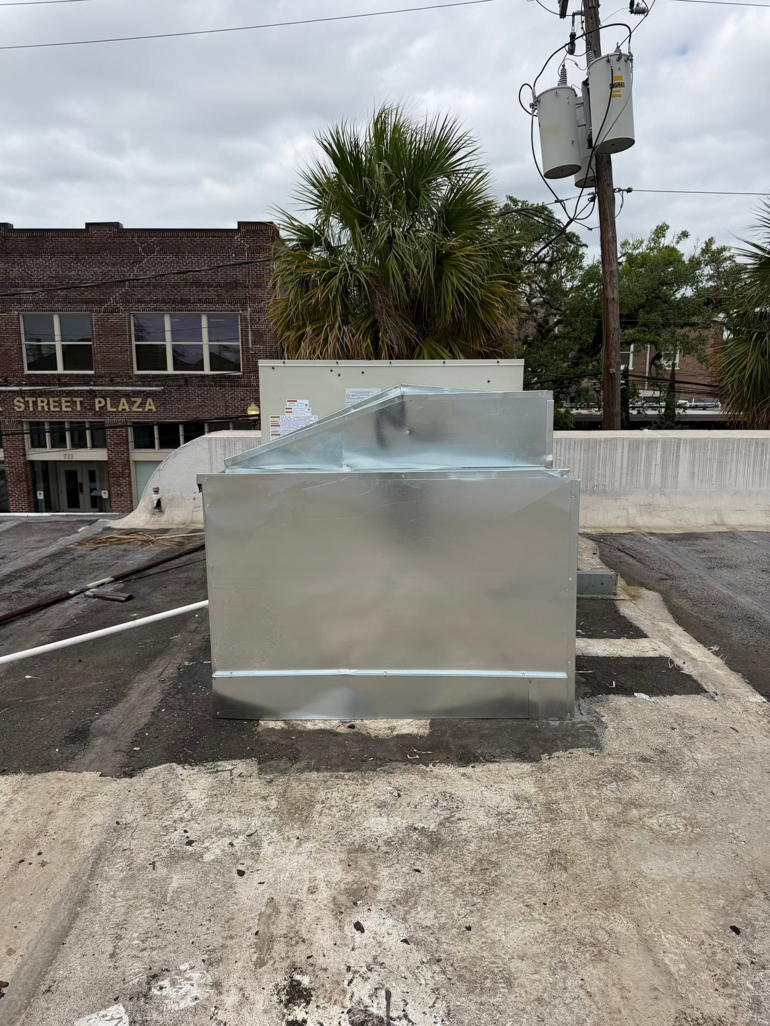 Metal utility box with a blue-gray fixture on a rooftop, with buildings and a utility pole in the background