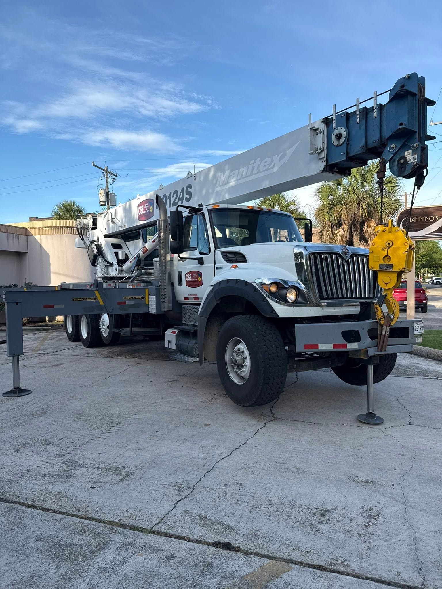 White utility crane truck parked on gravel under a blue sky, with an extended boom and outriggers deployed.