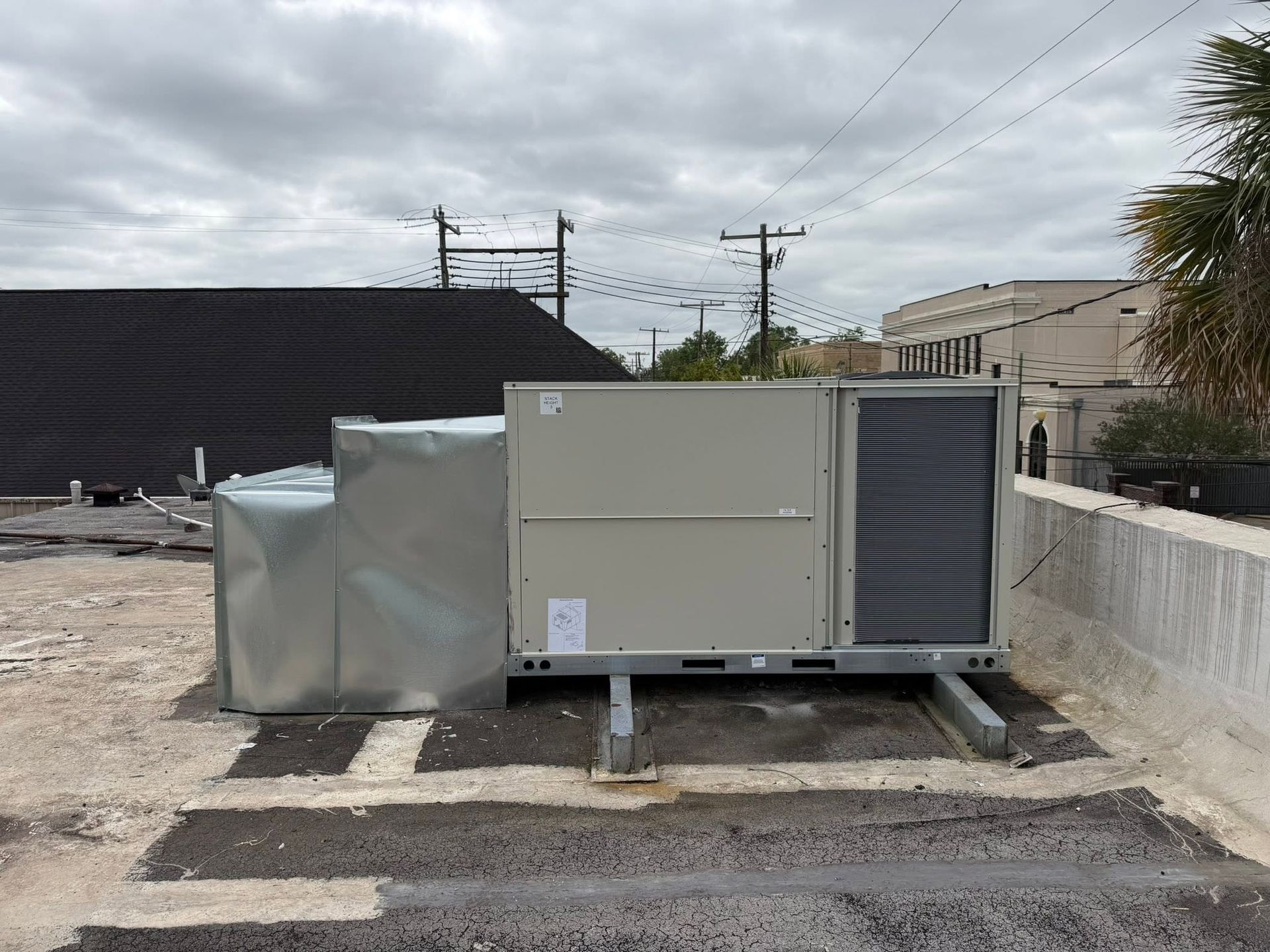 Large beige HVAC unit on concrete pads beside a building, outdoors under a cloudy sky