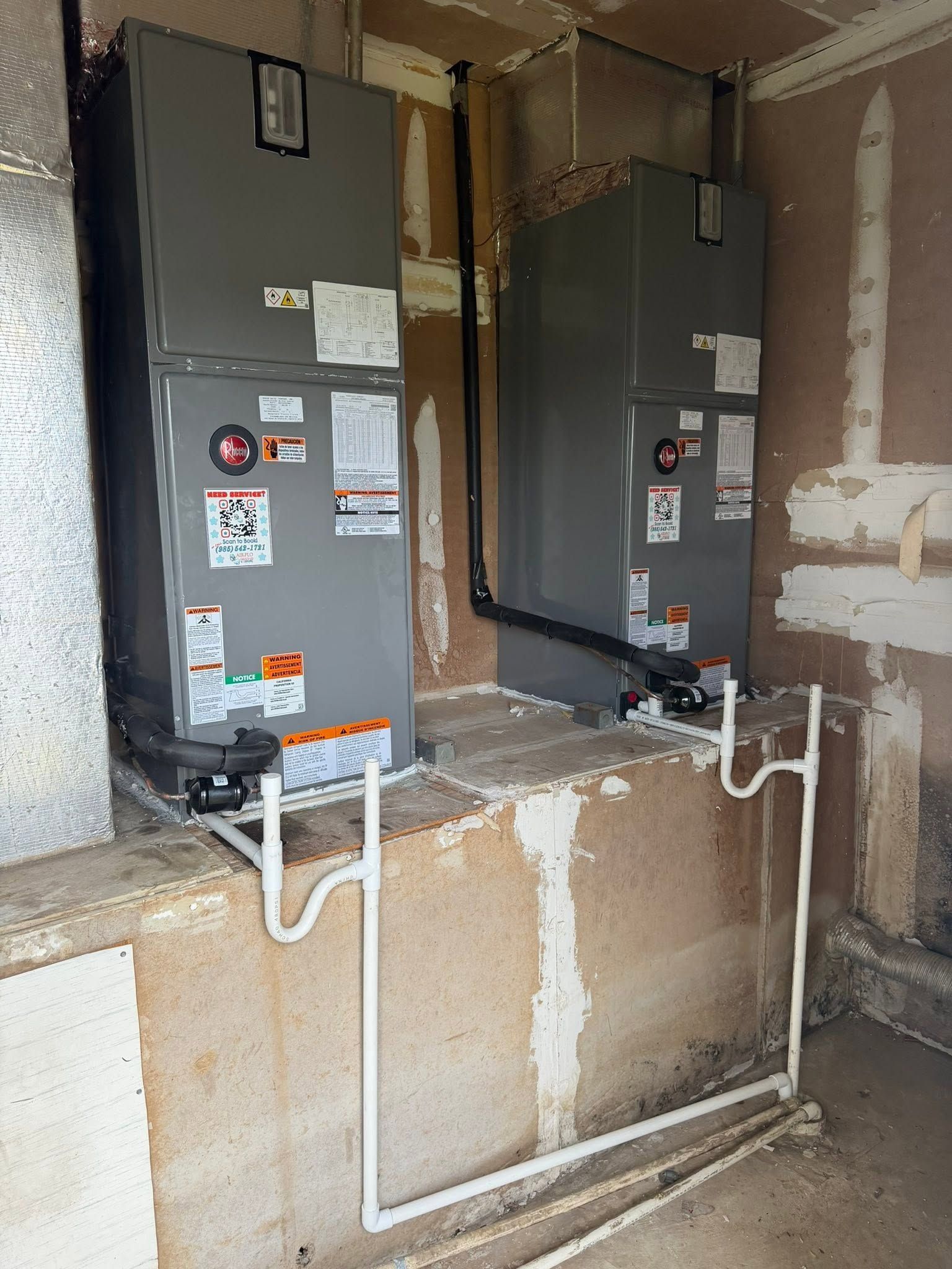 Two gray utility units with exposed pipes in a unfinished concrete utility room