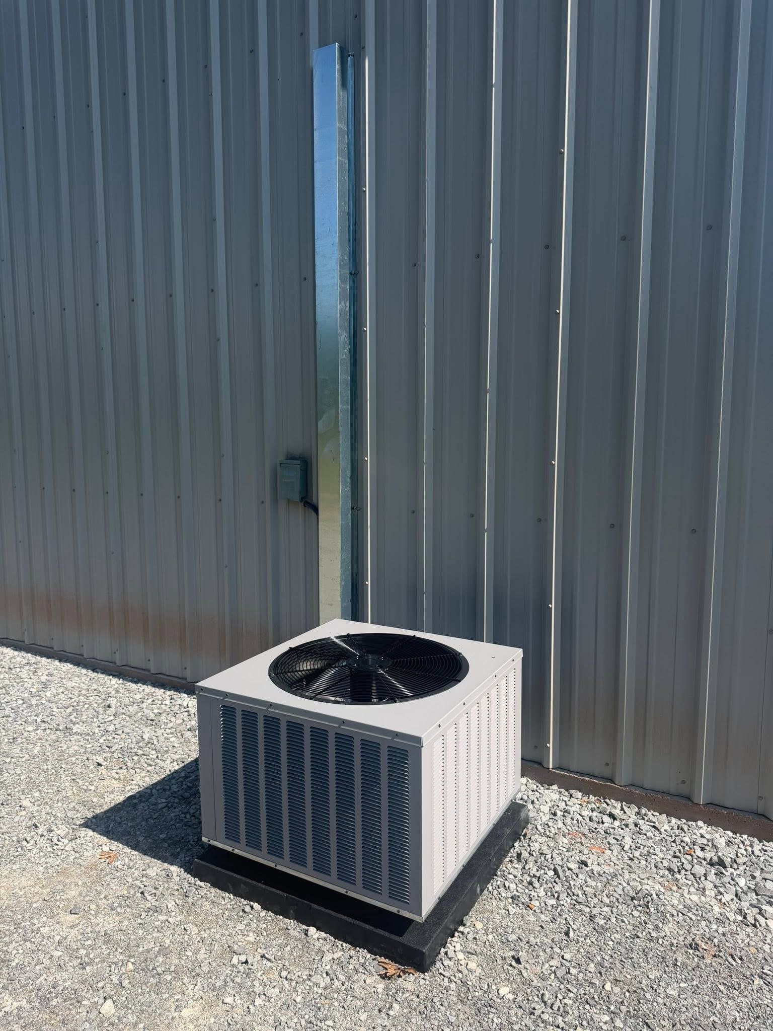Outdoor air conditioning unit beside a metal building wall on gravel.