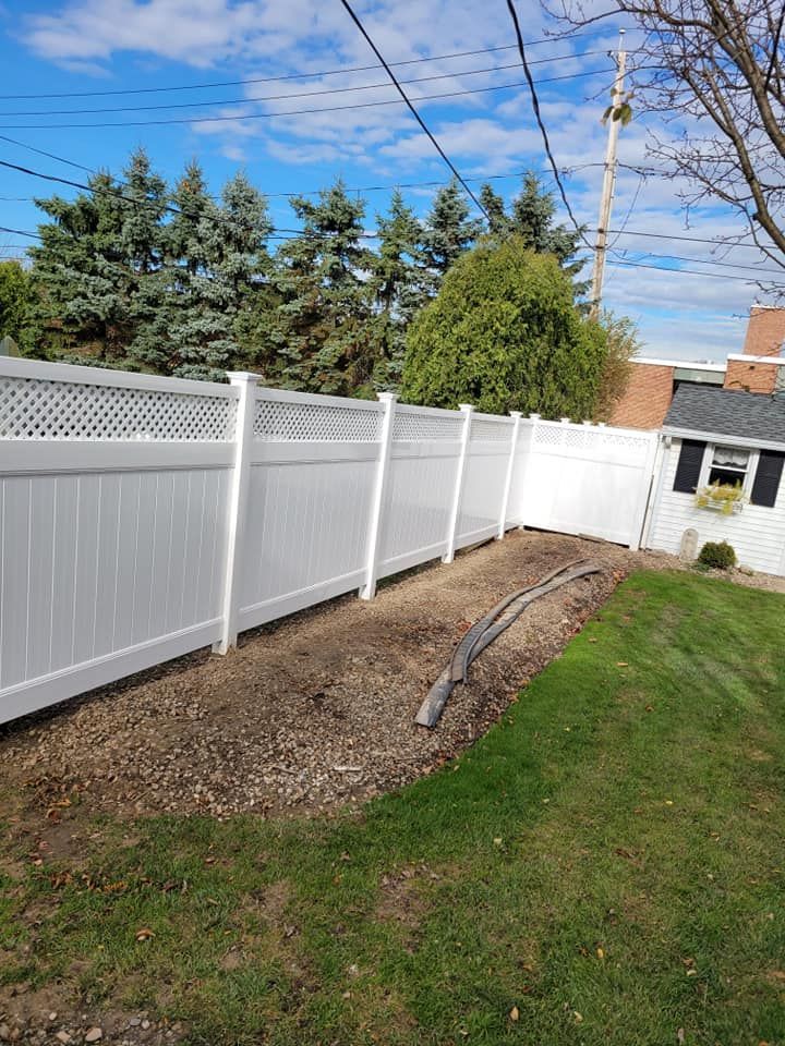 Backyard with a white vinyl fence, green lawn, mulch bed, and blue sky with power lines
