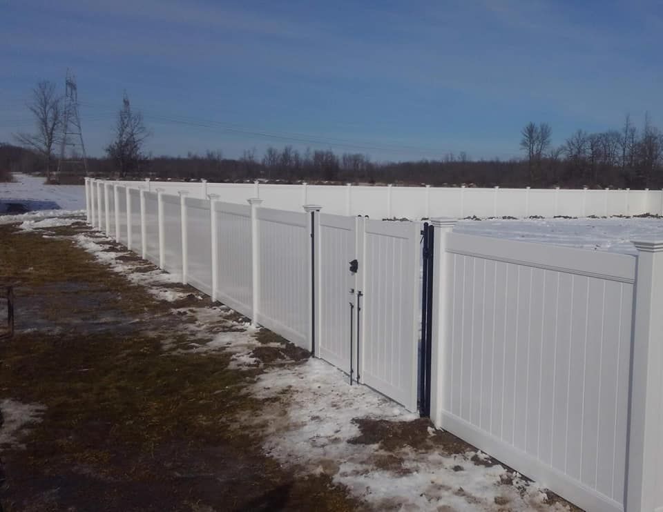 Long white fence with a gate along a snowy field under a clear blue sky