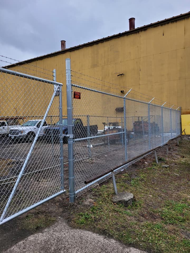 Chain-link fence beside a yellow industrial building and parked cars on a cloudy day