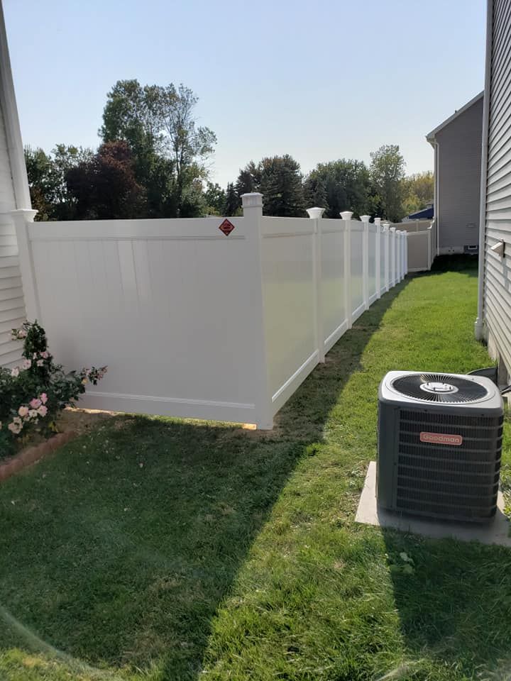 White vinyl privacy fence along a grassy side yard beside two houses, with an air conditioner unit in the foreground.
