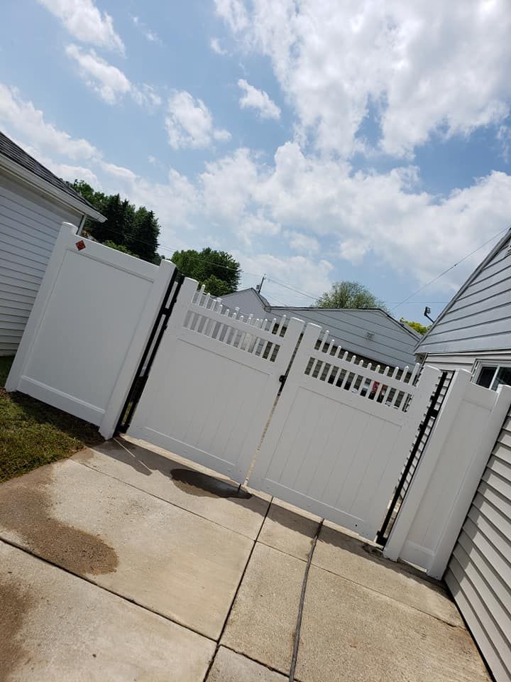 White storage shed panels and gate beside a gravel driveway under green trees on a sunny day