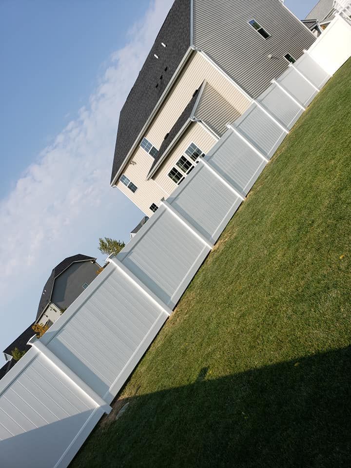 Suburban house and white vinyl fence beside a green lawn on a sunny day.