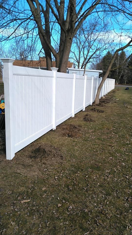 White vinyl fence and gate between two houses, with a shovel on the ground in a sunny yard.