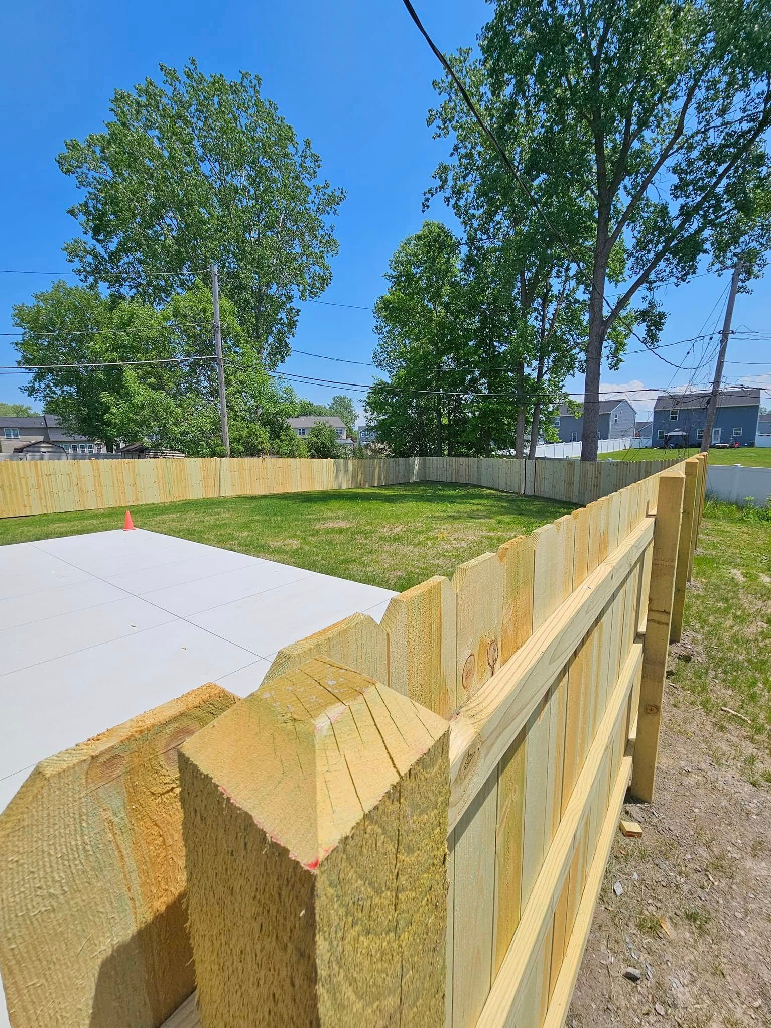 New wooden fence around a grassy yard with trees under a clear blue sky