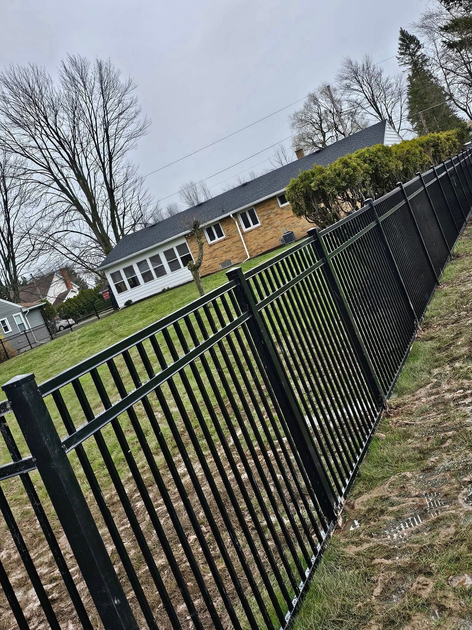 Black metal fence beside a grassy yard and brick building under a cloudy sky