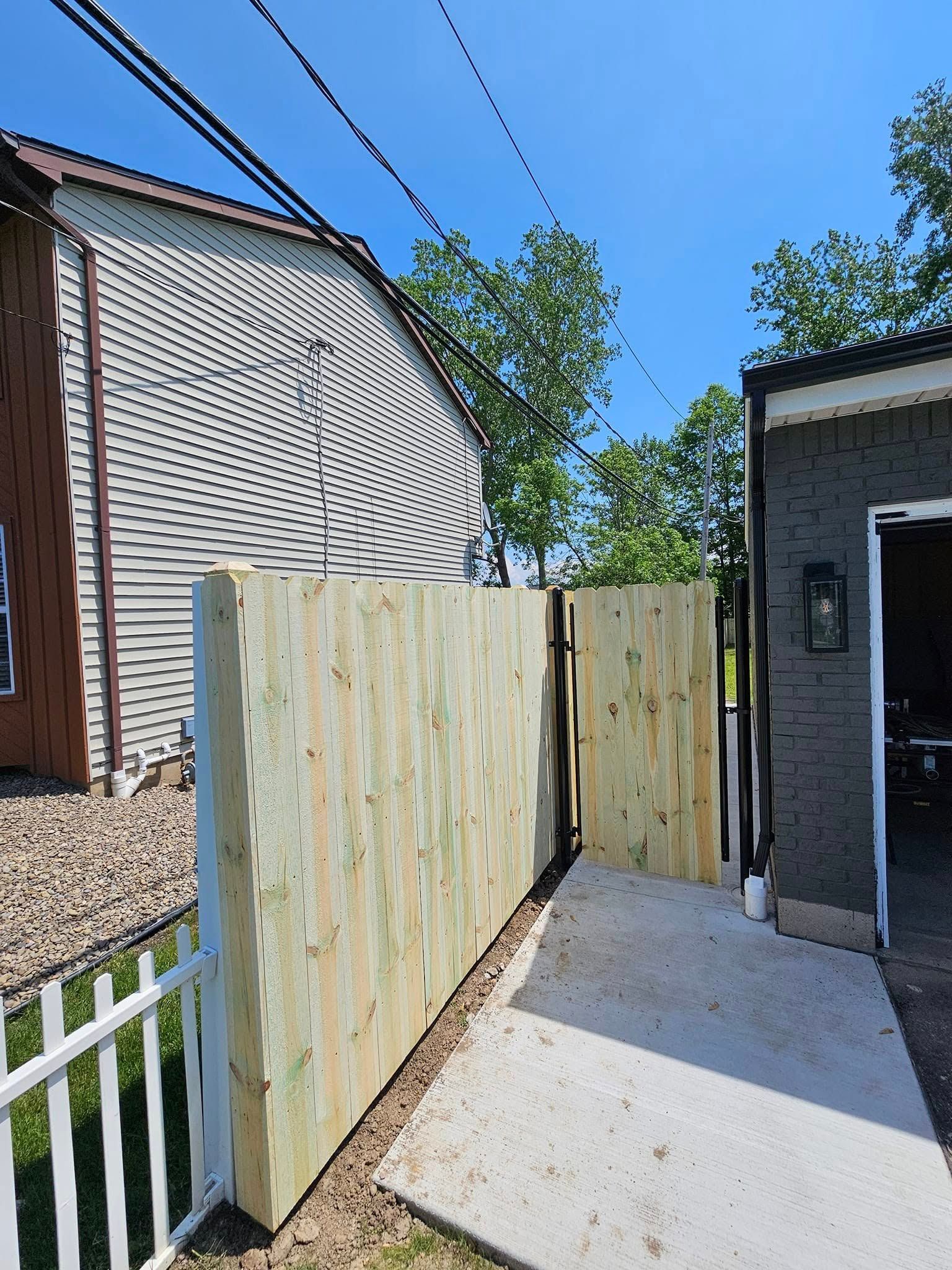 Narrow backyard passage with pale wooden fence, concrete path, and house walls under a blue sky
