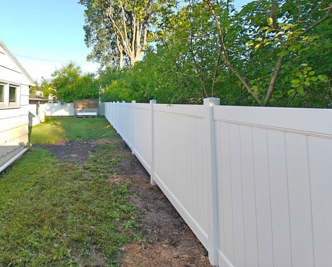 Backyard with a long white vinyl fence beside a grassy yard and trees