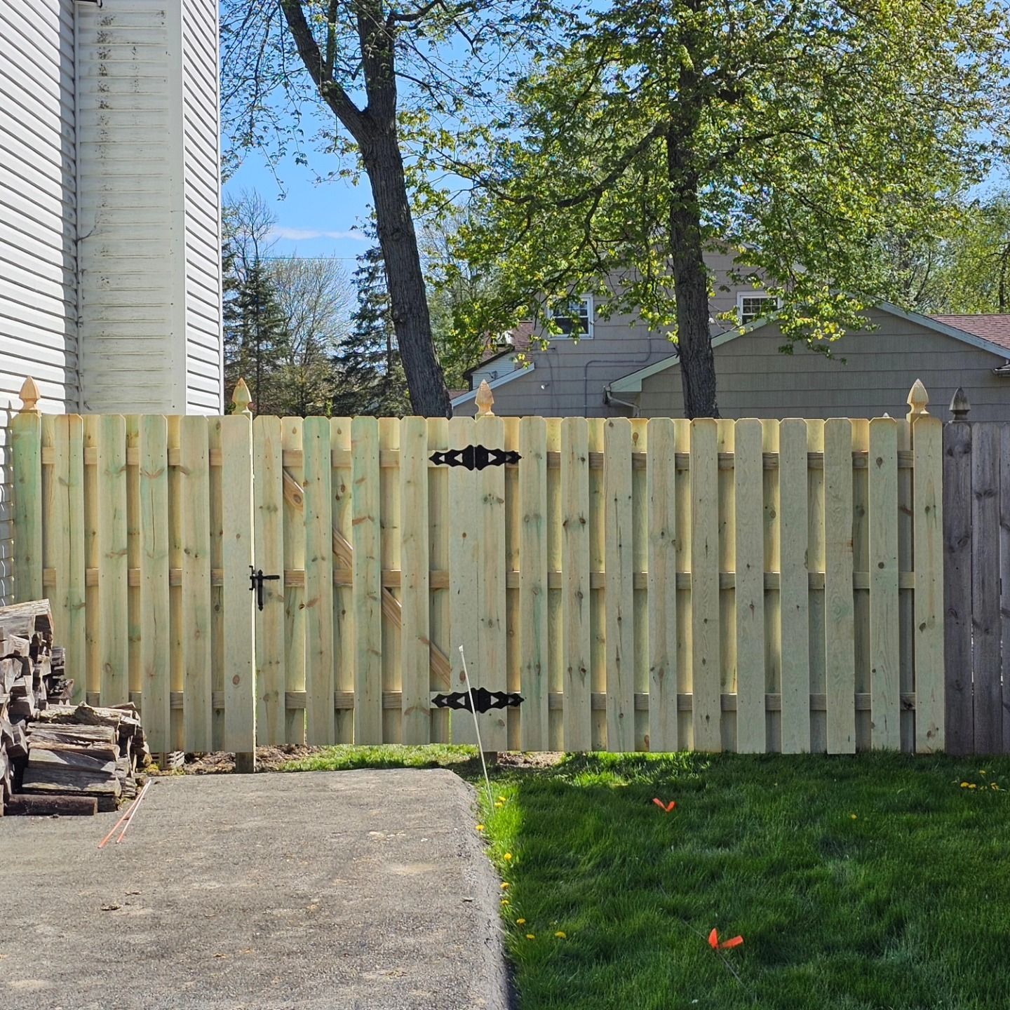 Wooden backyard gate in a fenced yard beside a concrete driveway and green lawn