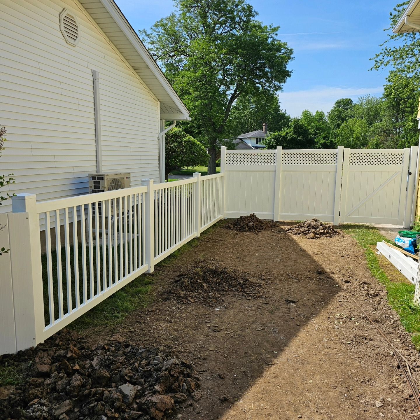 White fenced side yard with bare dirt path beside a house under a sunny sky.