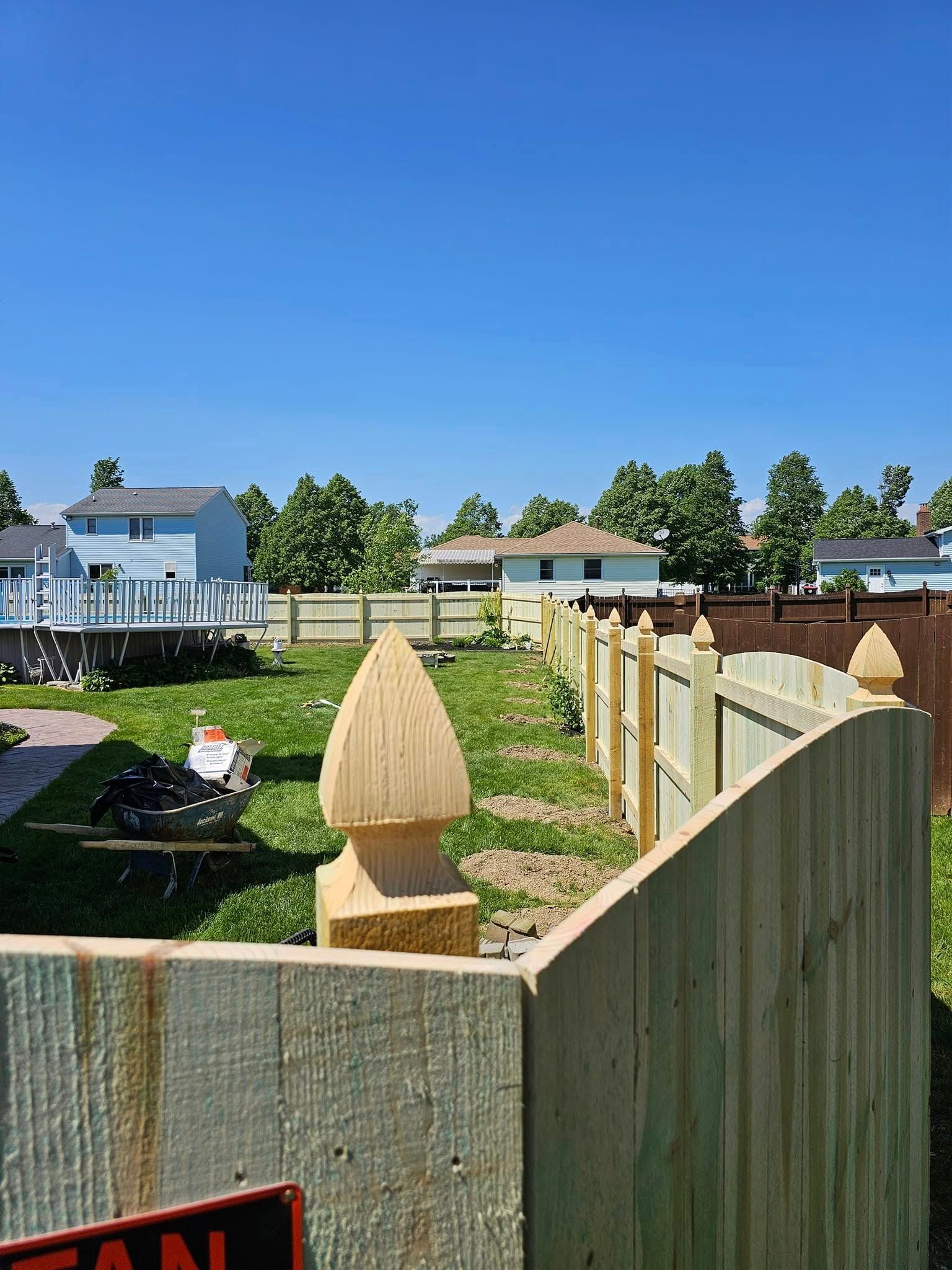 Wooden fence posts in a sunlit backyard garden with houses in the background under a blue sky