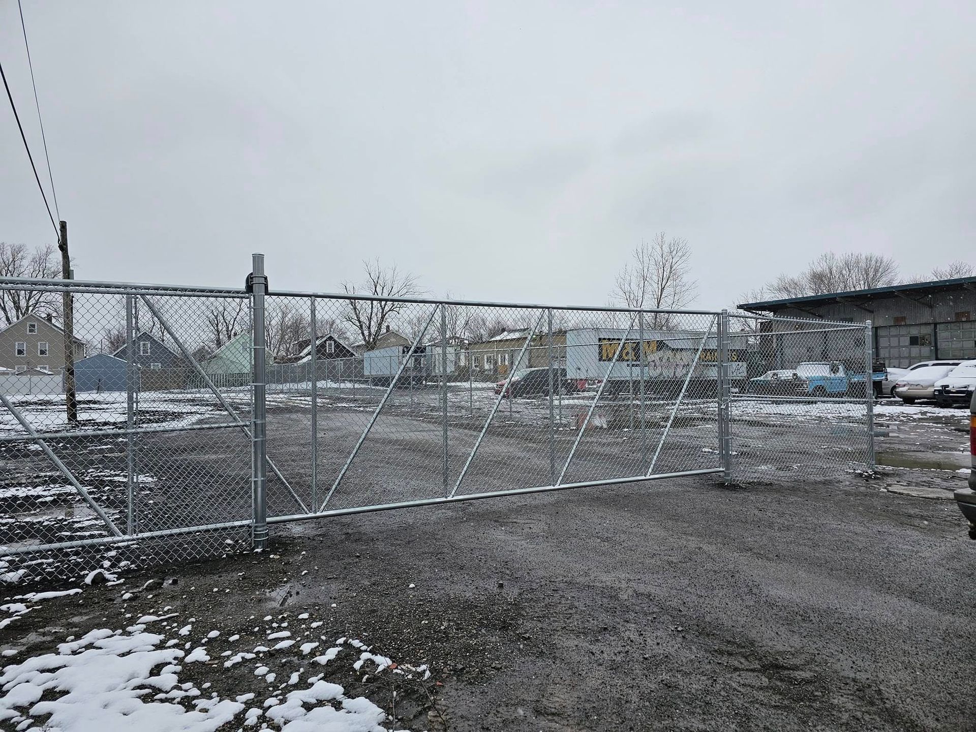 Chain-link gate across a snowy gravel lot on an overcast day