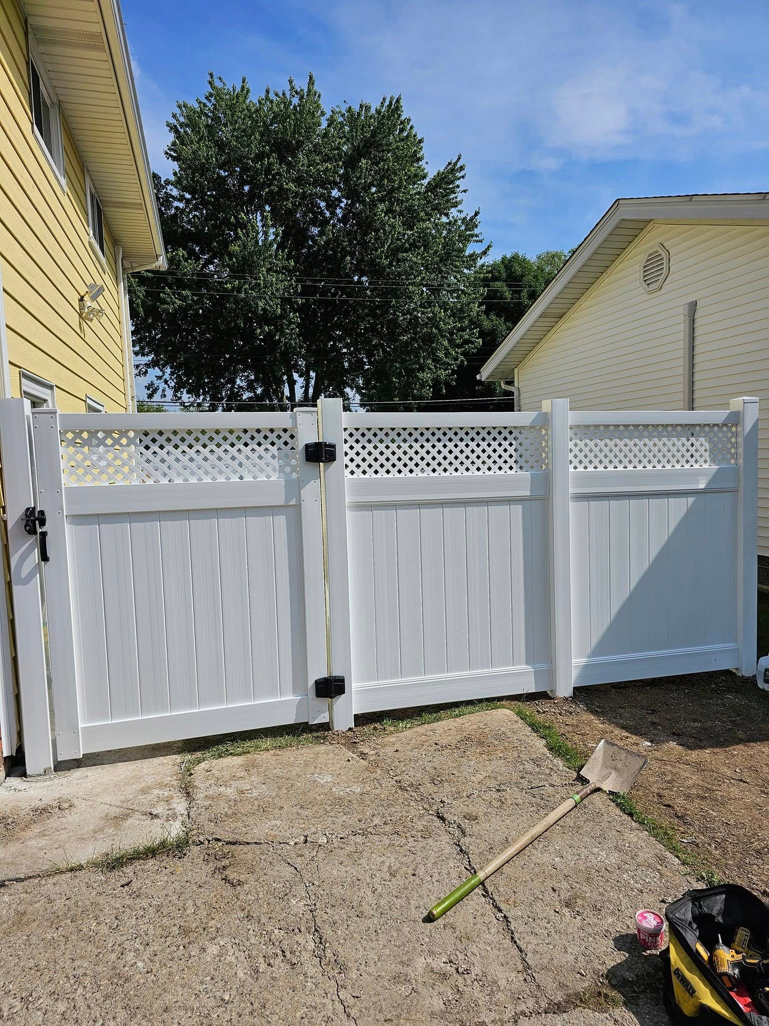 White vinyl fence with gates between two yellow houses, with a tree visible behind it.