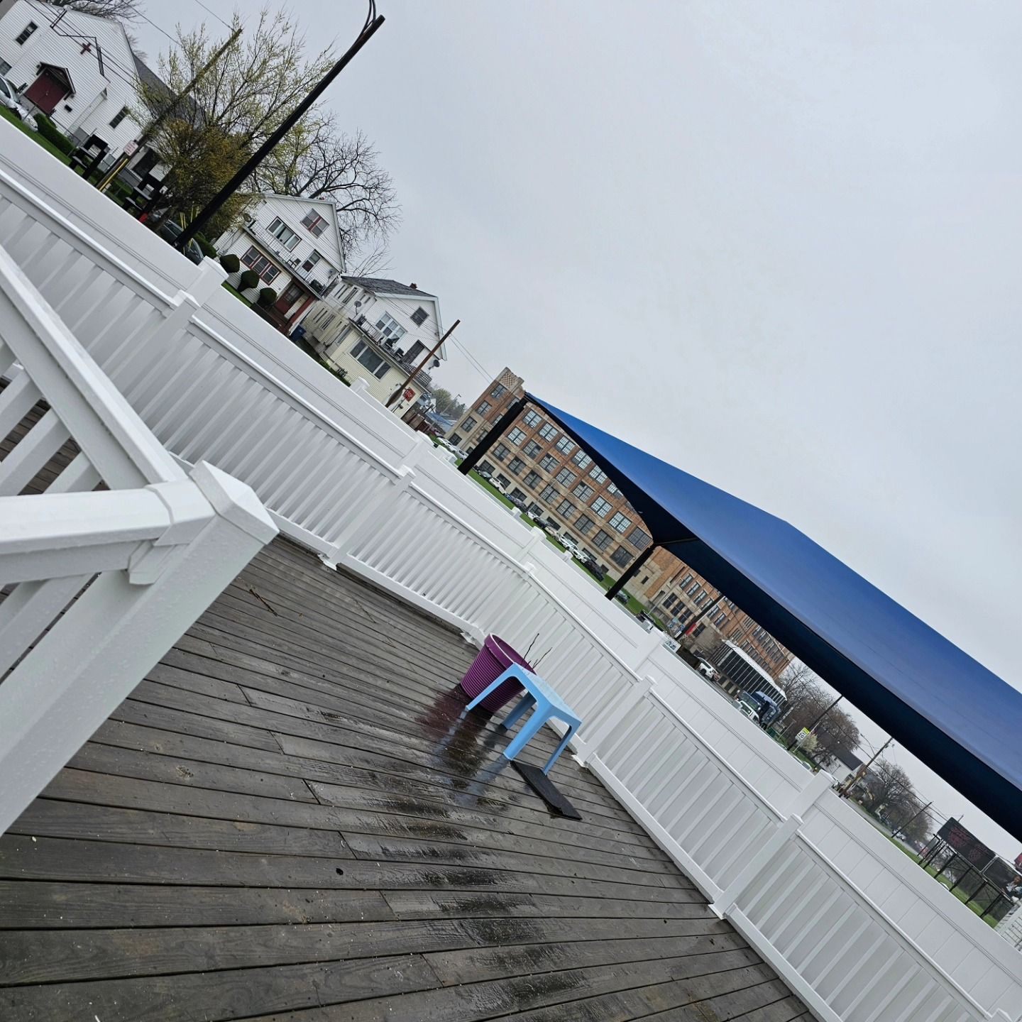 Tilting view of a white boardwalk deck with railings, a blue awning, and a small colorful table near the center