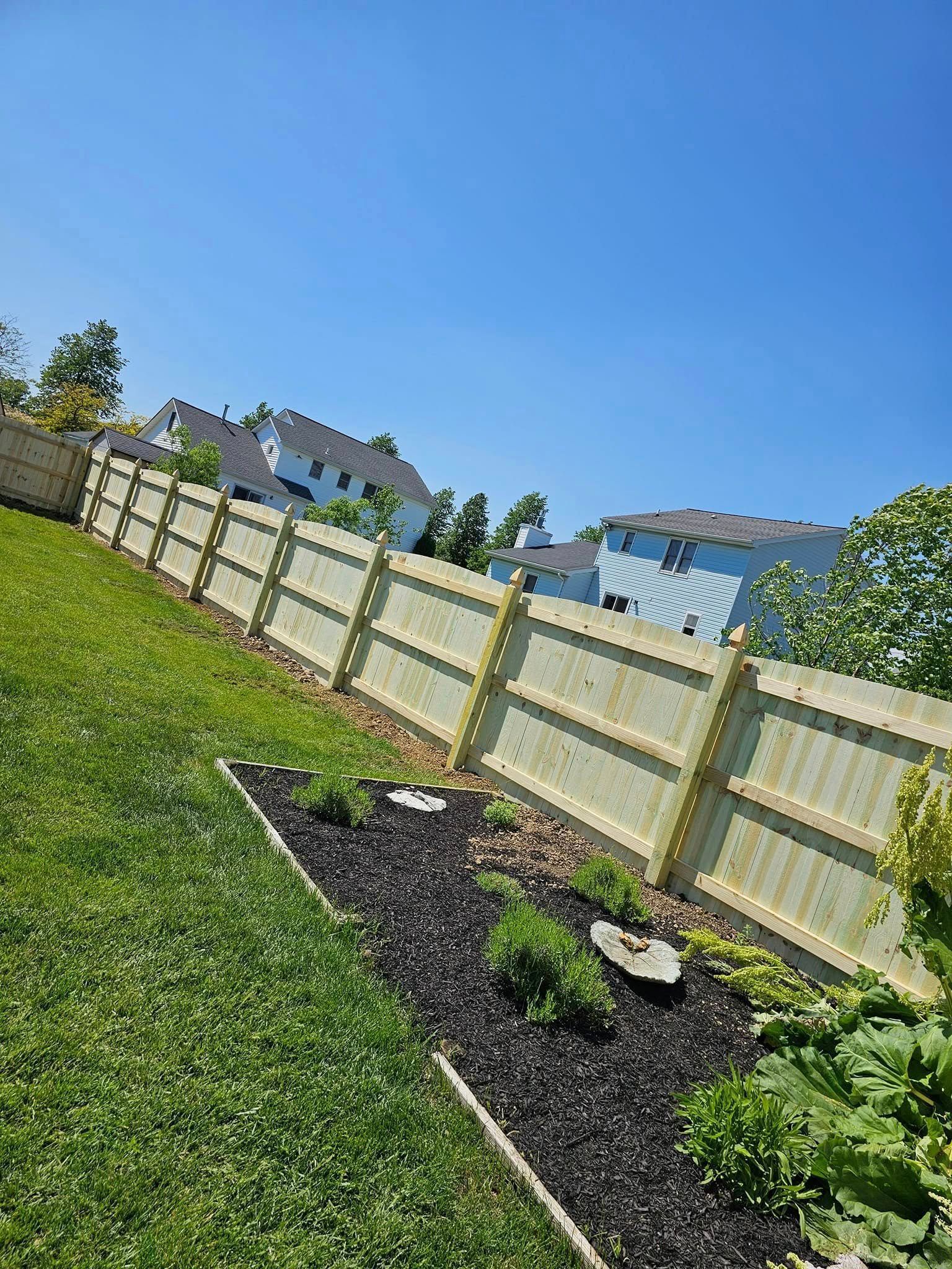 Backyard garden bed with young plants beside a white fence under a clear blue sky