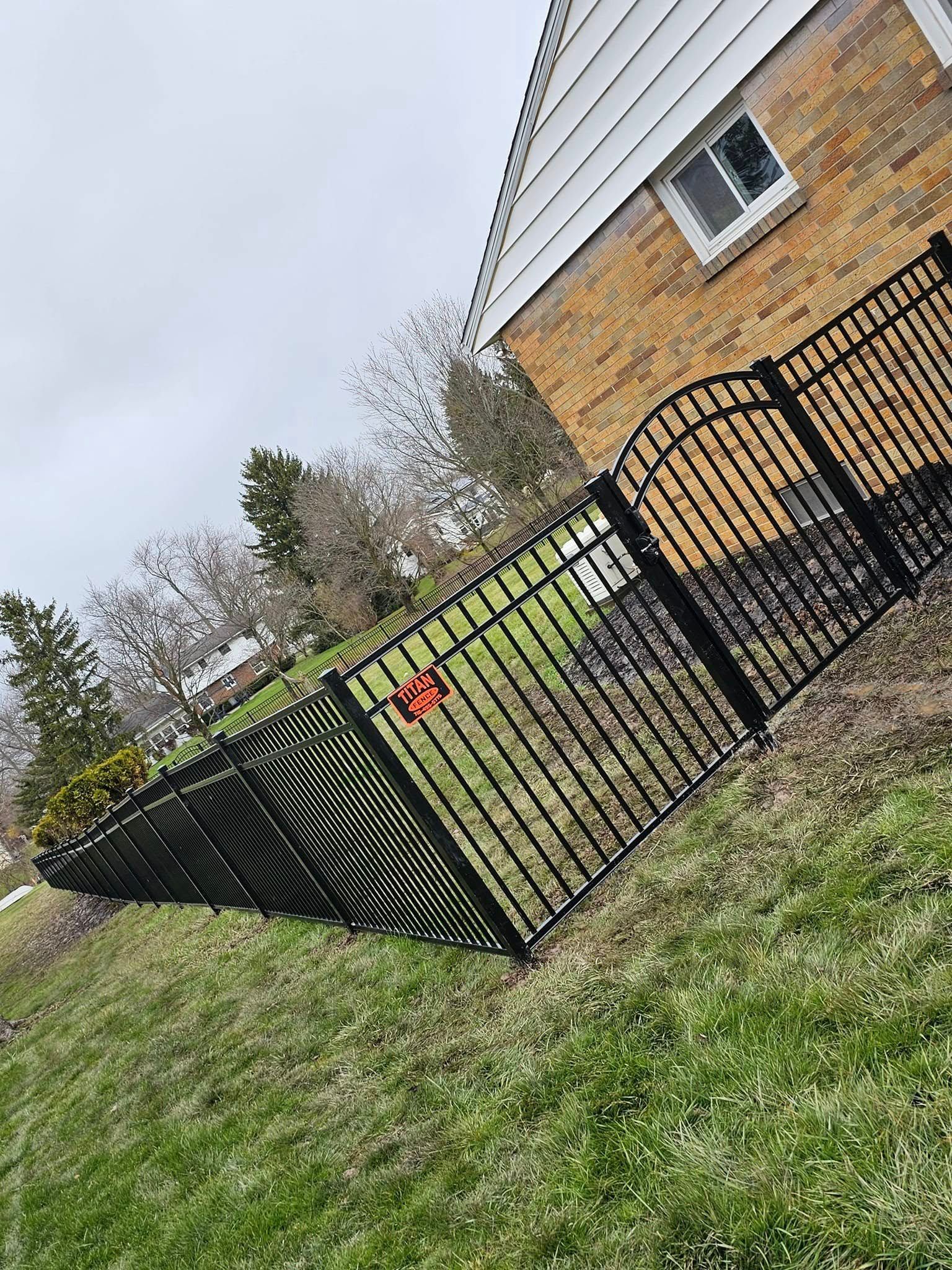 Black metal fence beside a brick house and grassy yard on a cloudy day