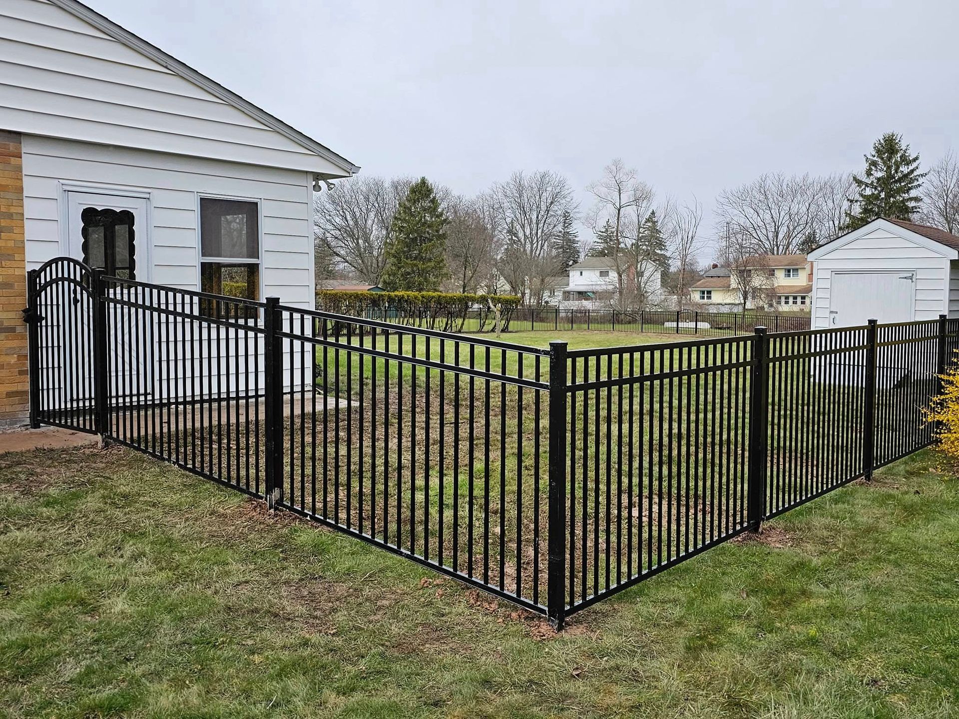 Black metal fence enclosing a grassy yard beside a white house
