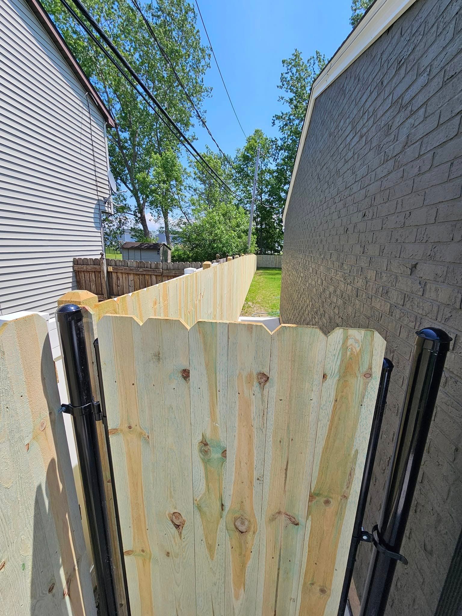 Wooden gate between two houses, opening to a backyard with a grassy path and trees.