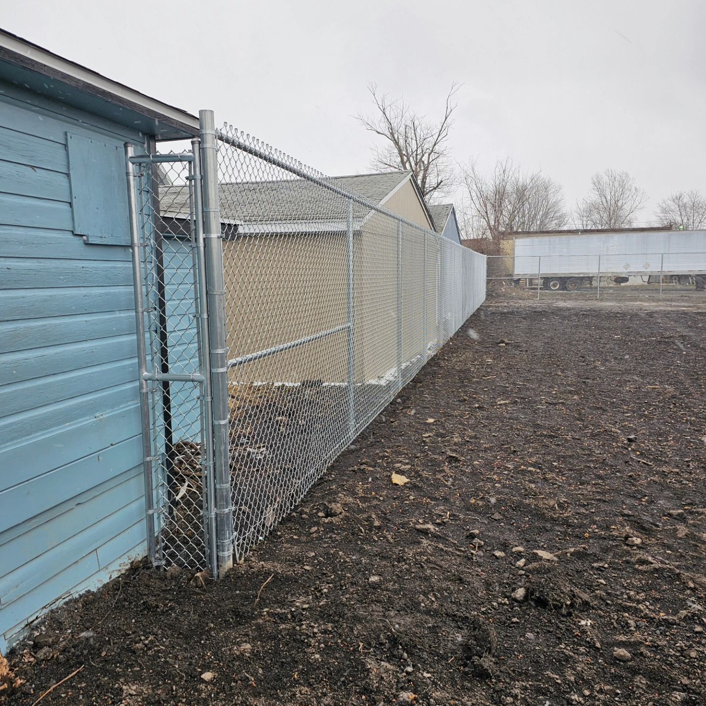 Blue shed beside chain-link fence along a gravel yard under an overcast sky