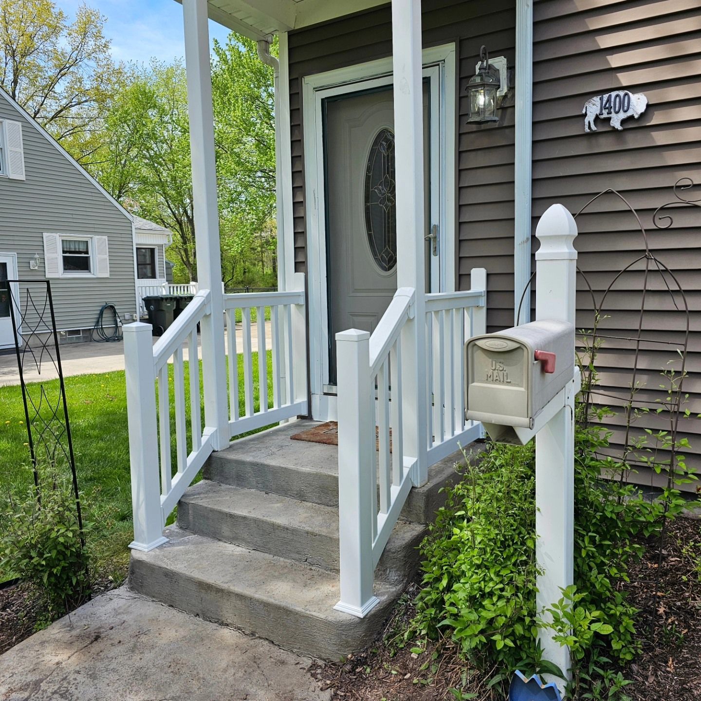 Front porch with concrete steps, white railings, gray siding, and a white mailbox by the door