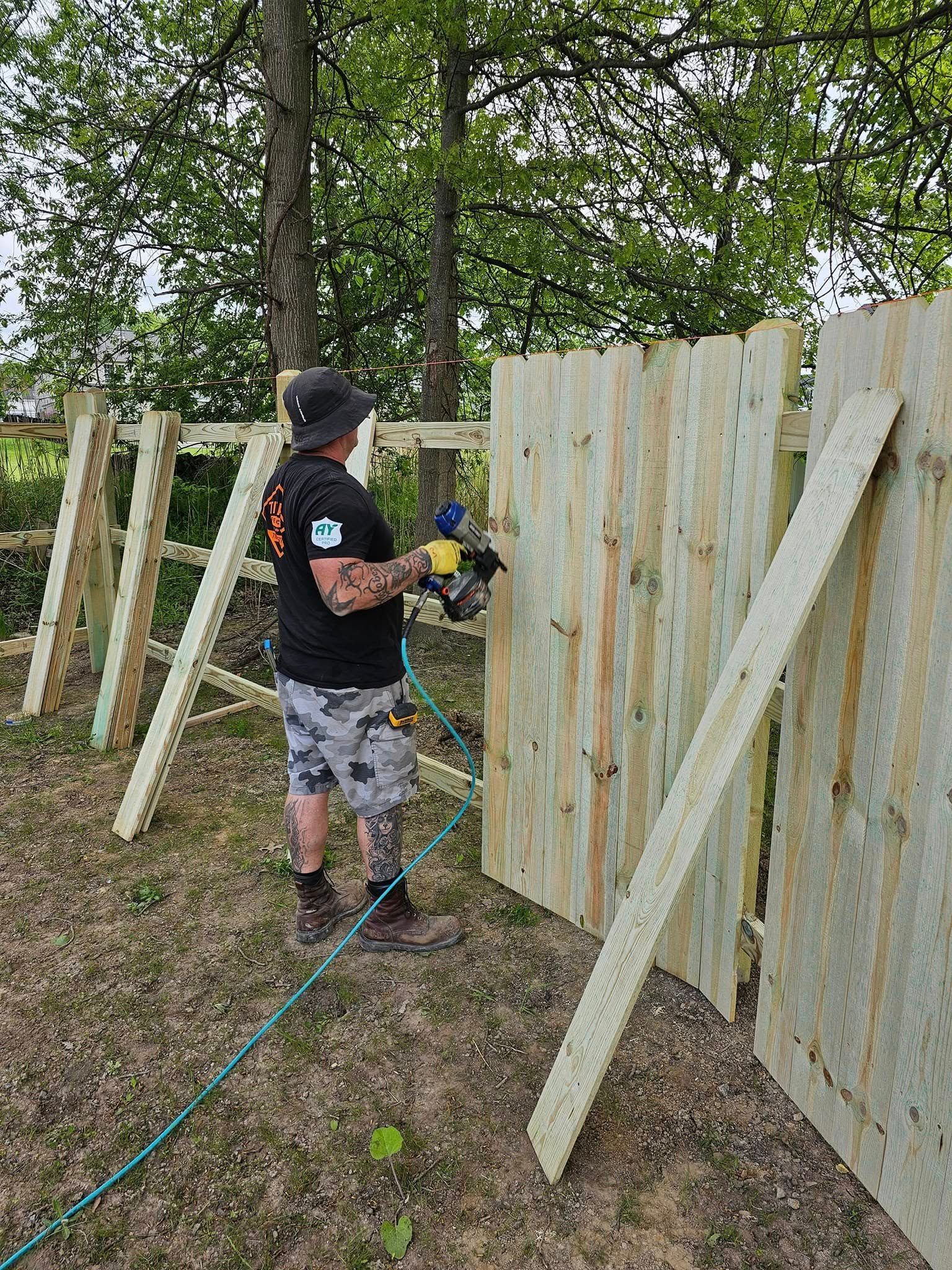 Person using a power drill to build a wooden fence outdoors.